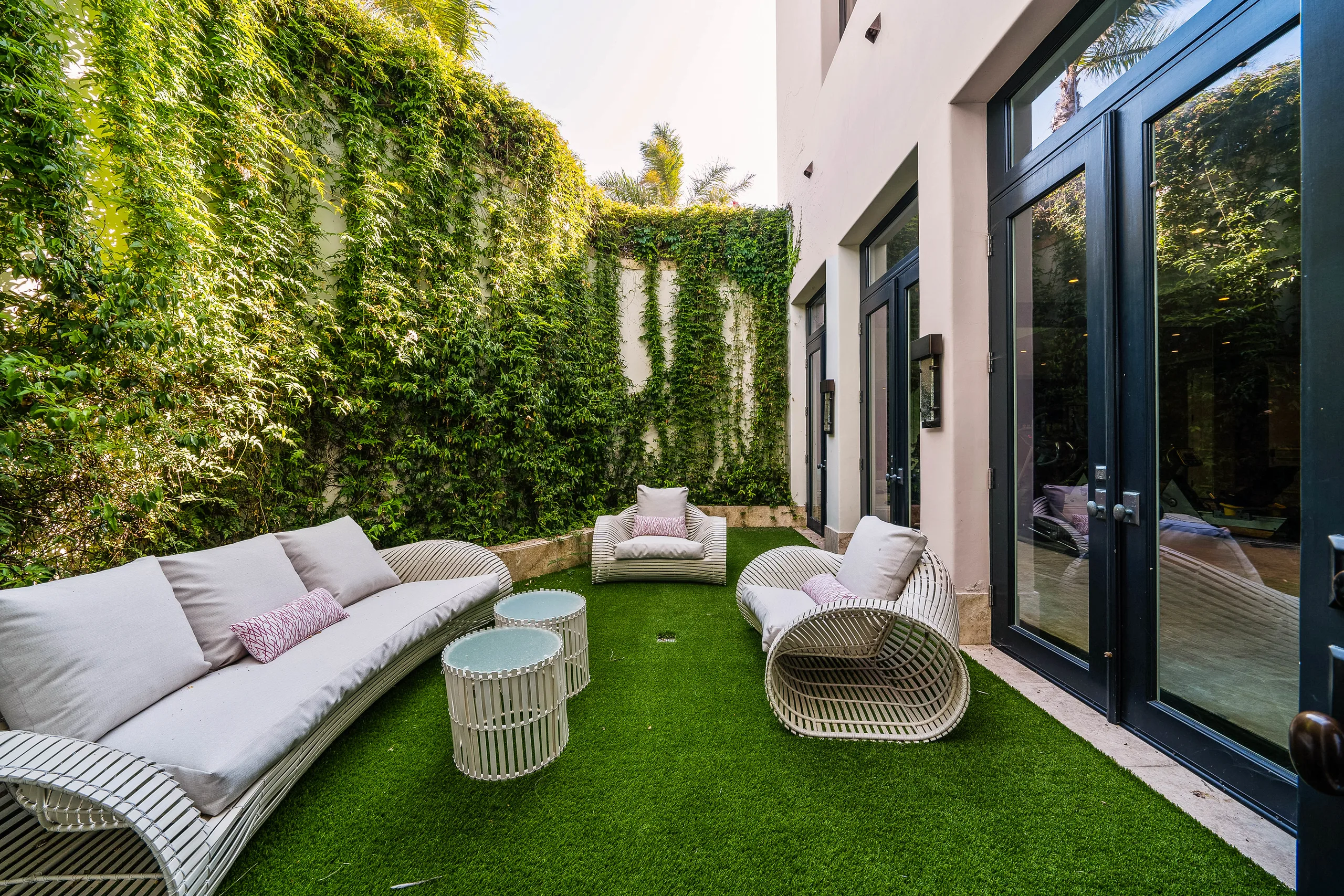 Sheltered side courtyard on artificial lawn, woven daybeds and armchairs against a wall of climbing greenery