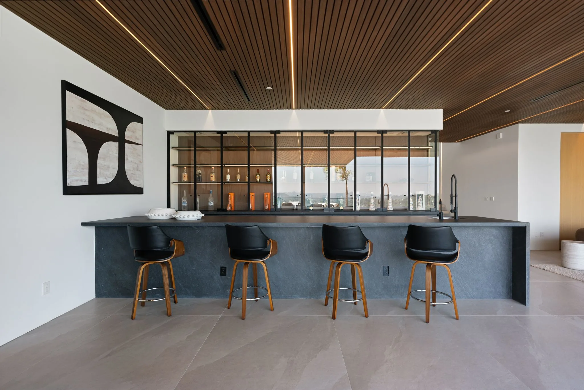 Charcoal stone bar counter with four leather swivel stools and backlit bottle shelving