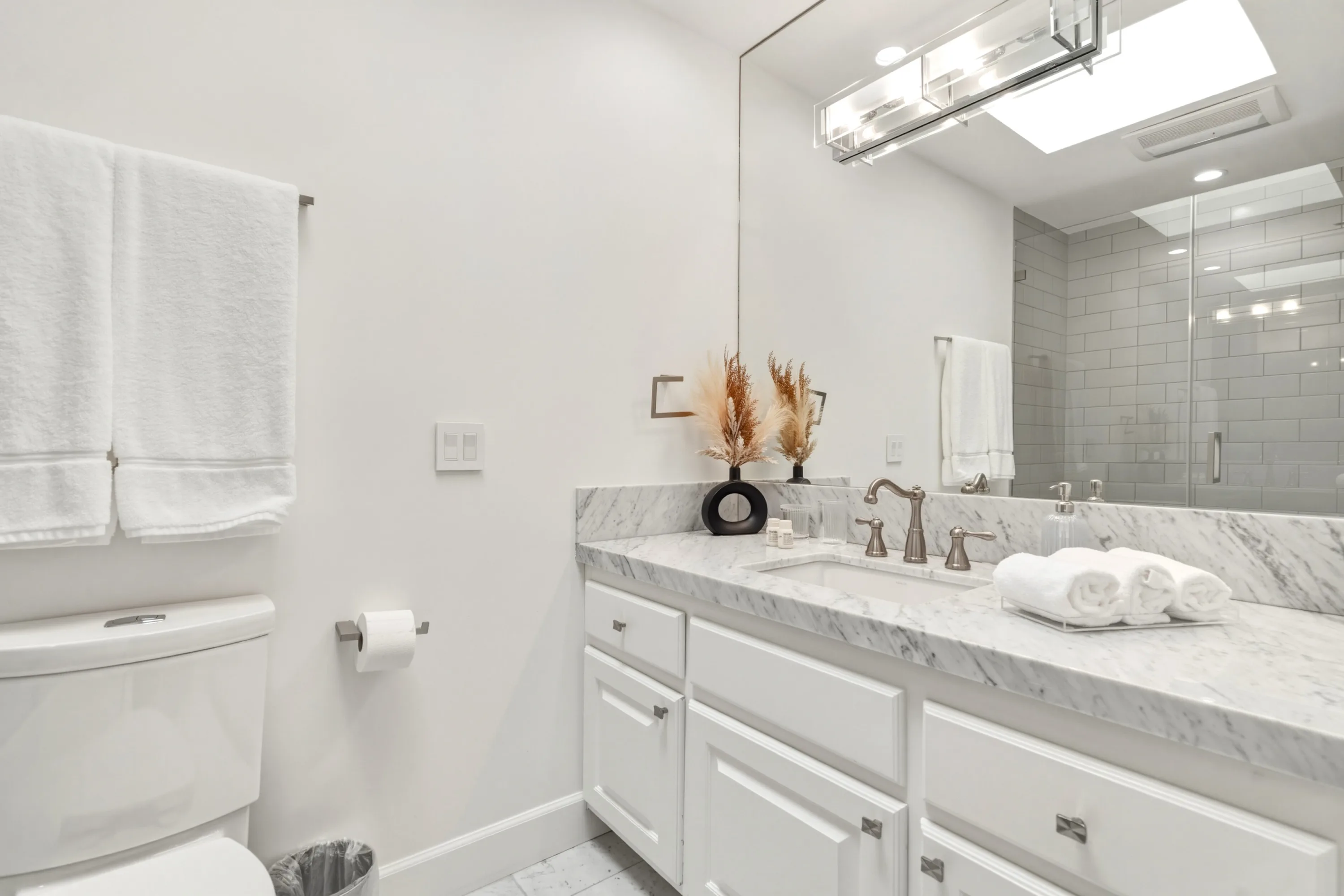 Bright bath with veined marble counter, dried pampas stems and skylit shower beyond