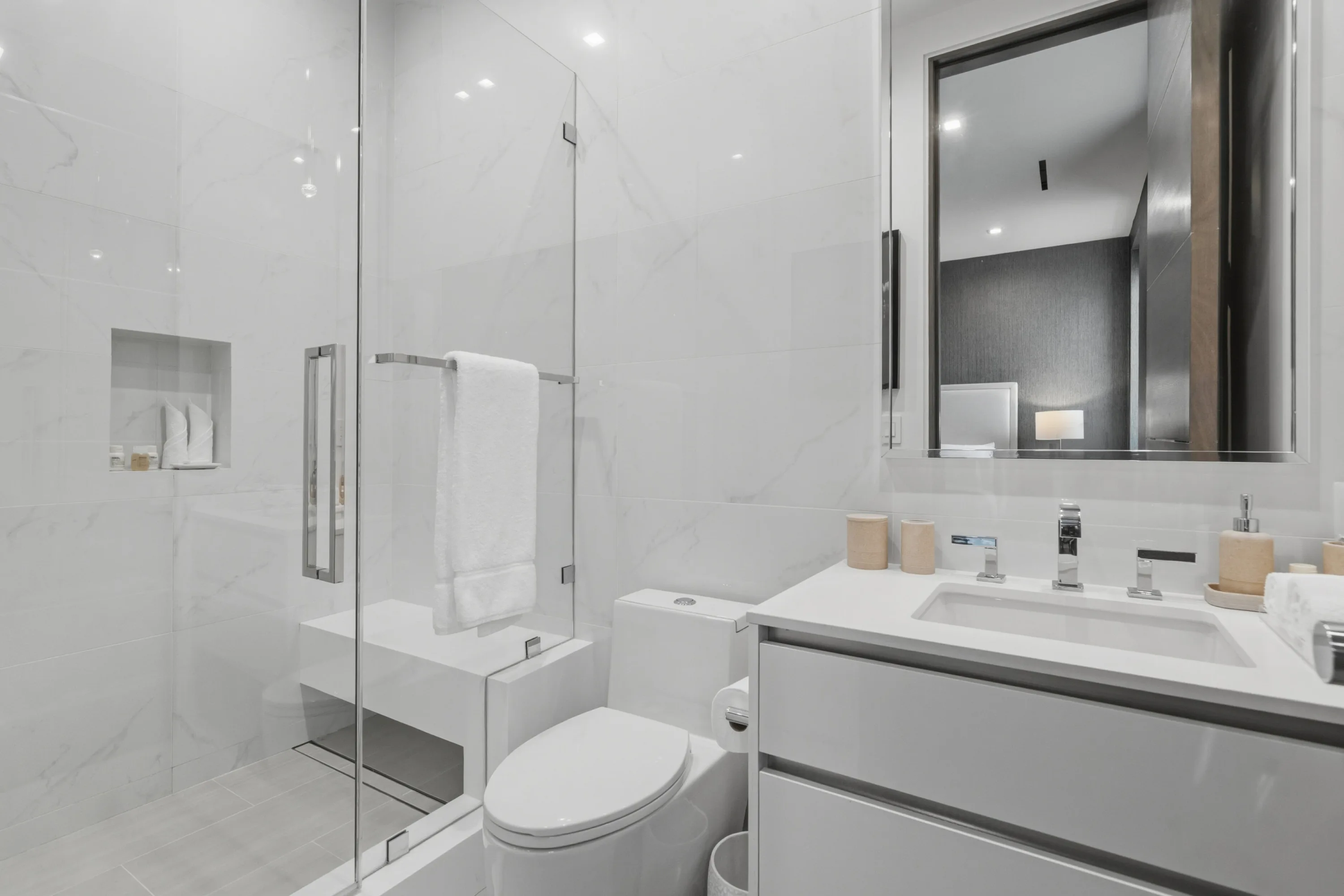 Marble-clad ensuite with walk-in glass shower, bench seat and streamlined vanity beneath a backlit mirror