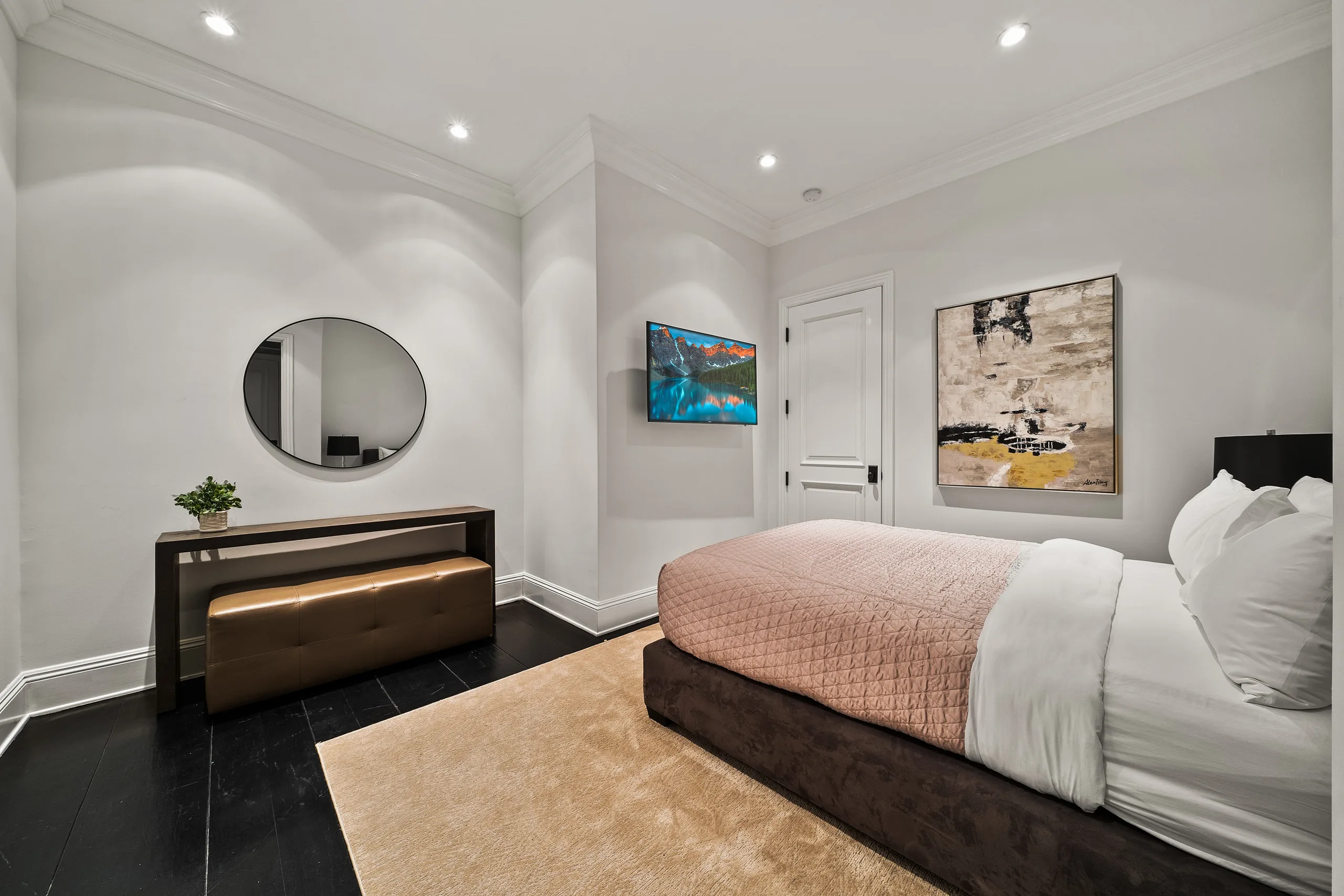 Guest bedroom in soft greys, blush quilted bed on dark timber floors, round mirror and abstract canvas