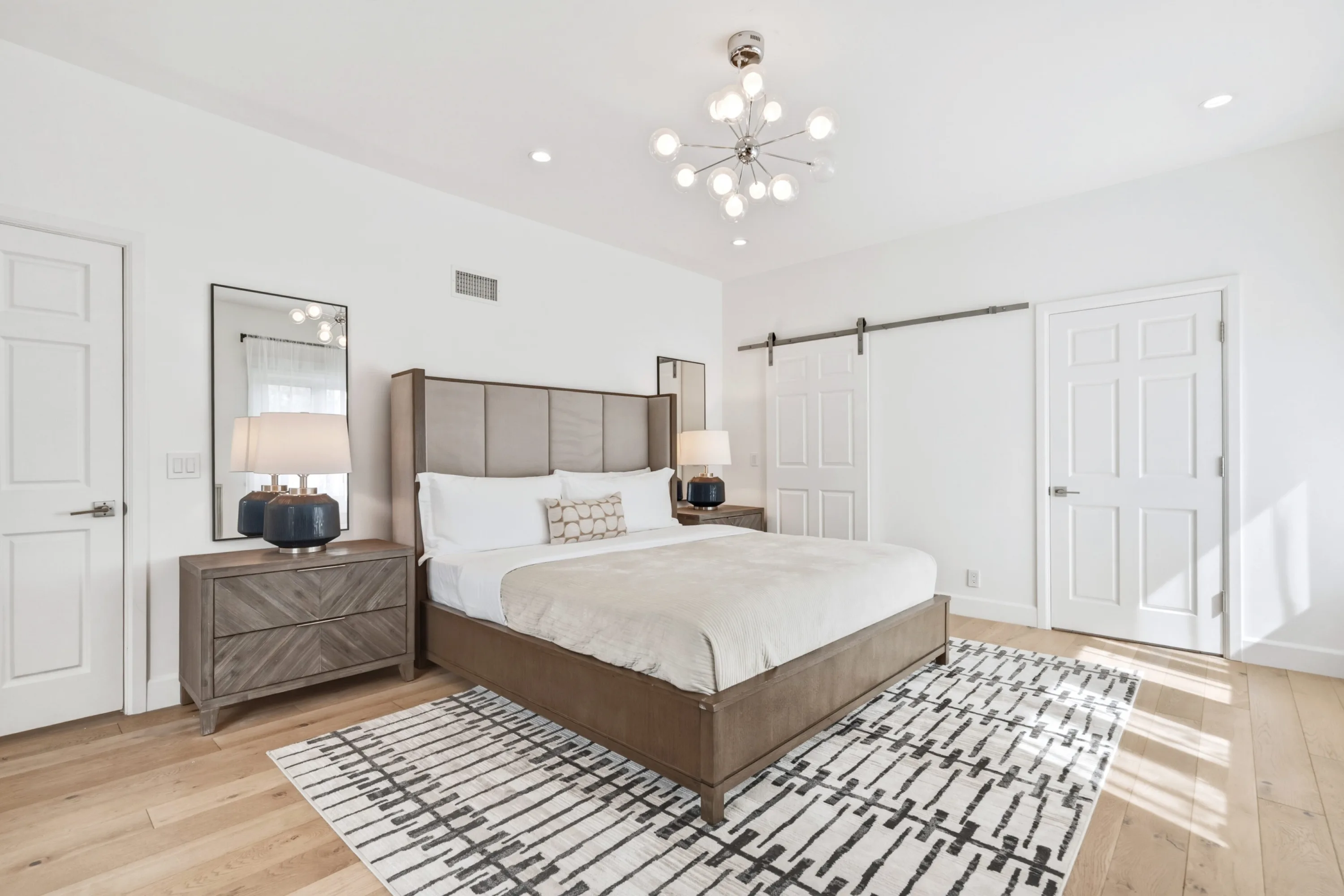 Sunlit bedroom with wood-framed bed, herringbone nightstand and barn door to the closet