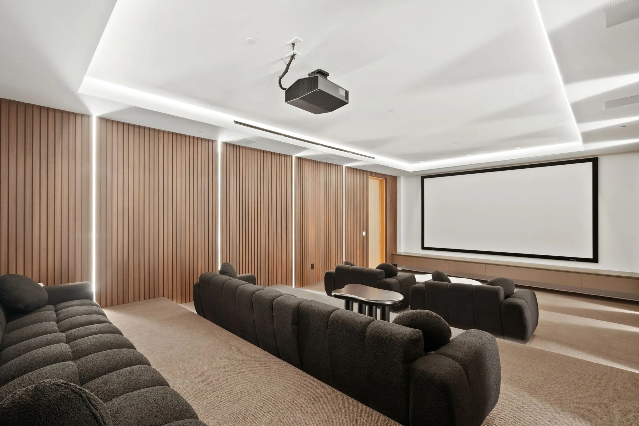 Home cinema with projector, wide screen and tiered rows of deep charcoal bouclé sofas against timber-slatted walls