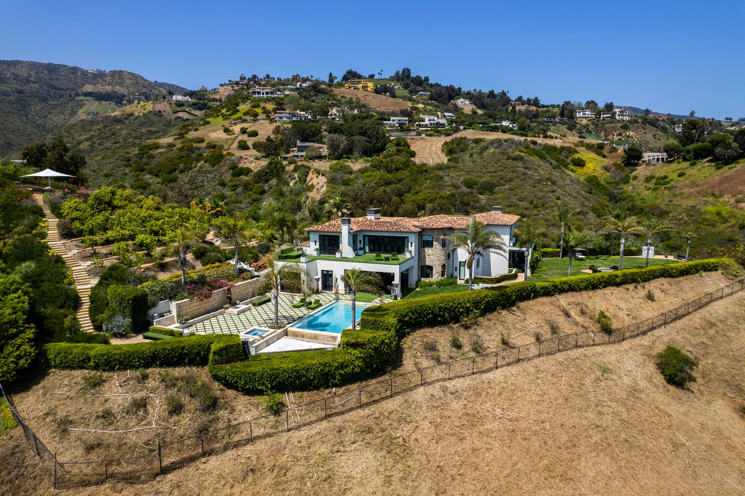 Aerial over the tile-roofed estate, pool and spa terraced into the Malibu hillside above open canyon