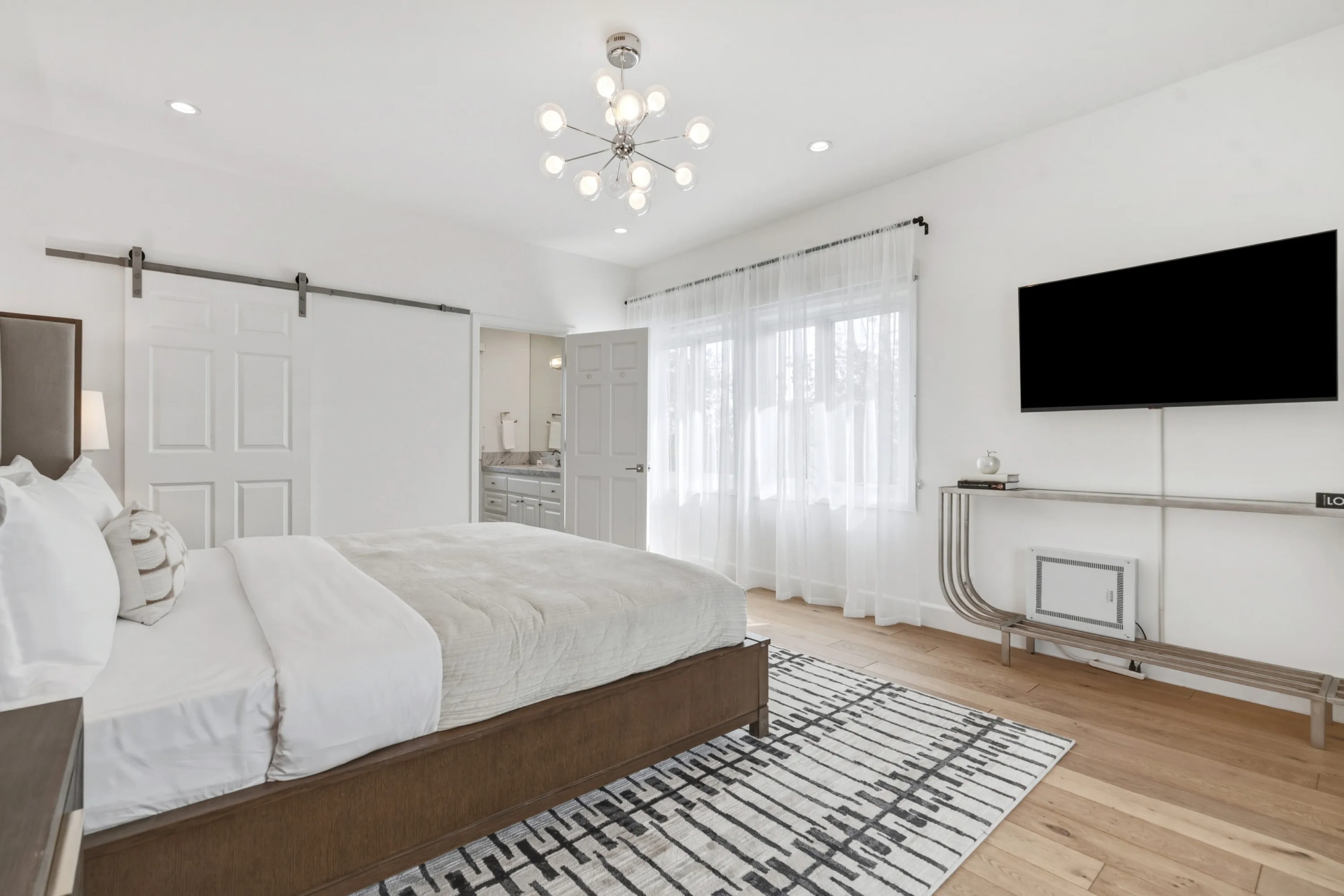 Bedroom with sliding barn door, curtained garden window and view into its private bathroom