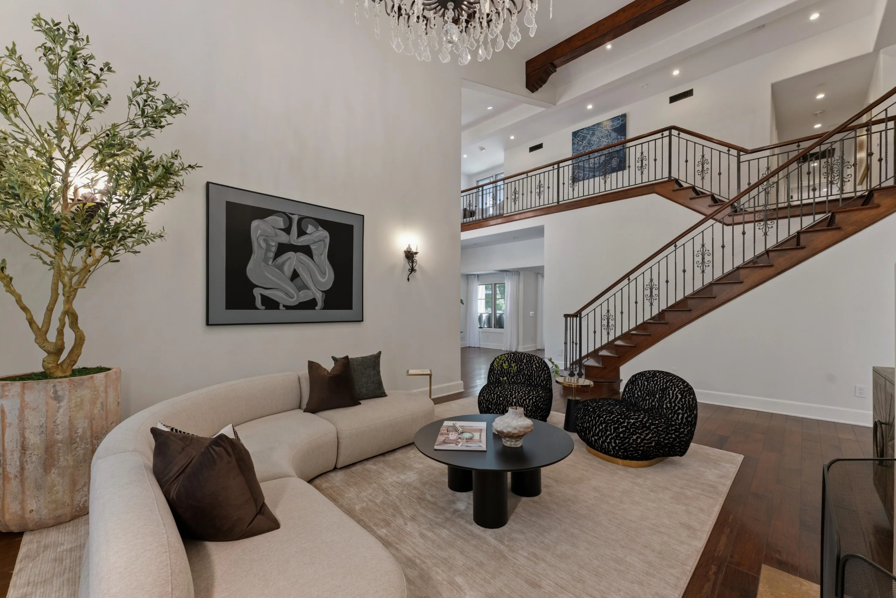Seating area with curved sectional and printed swivel chairs beside the sweeping staircase