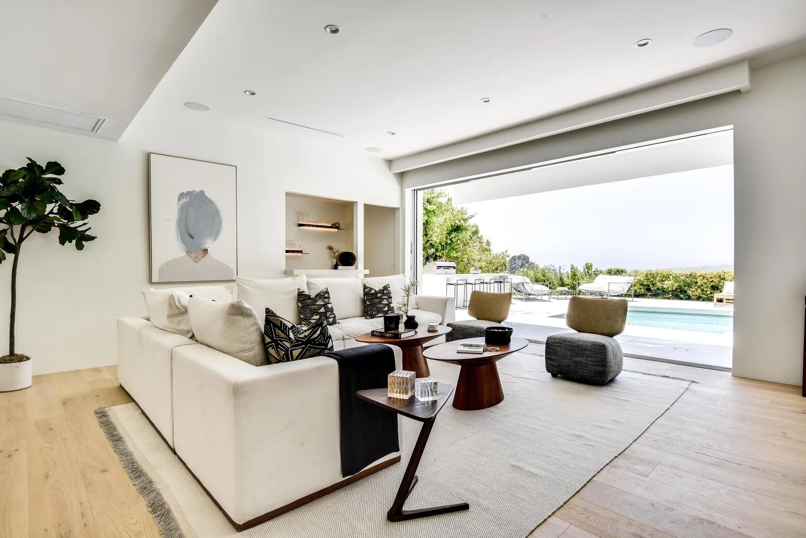 Sitting area with walnut nesting tables and olive stools, sliding doors folded back to the poolside