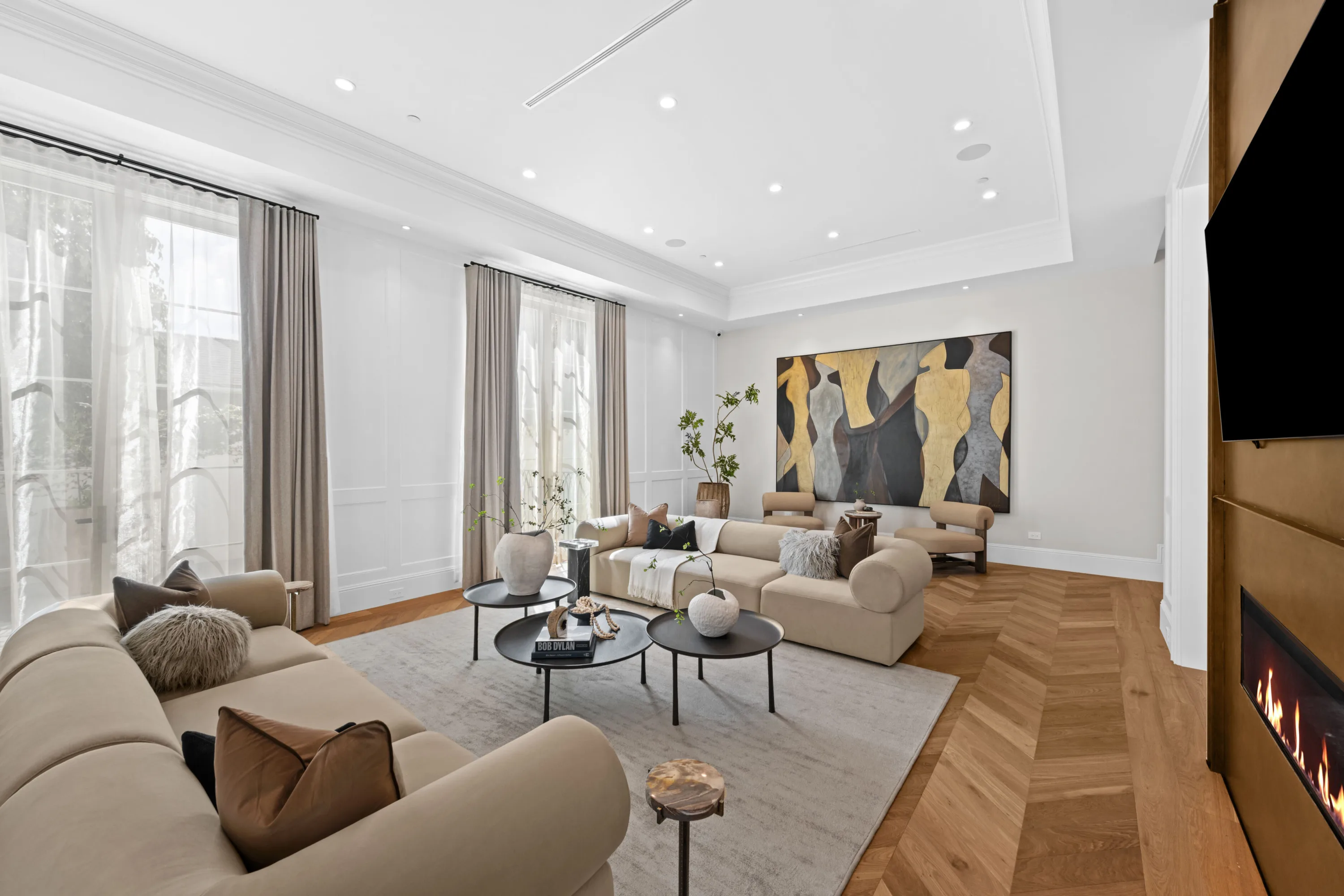 Formal sitting room with twin sofas, large abstract canvas and lit fireplace above herringbone oak floors