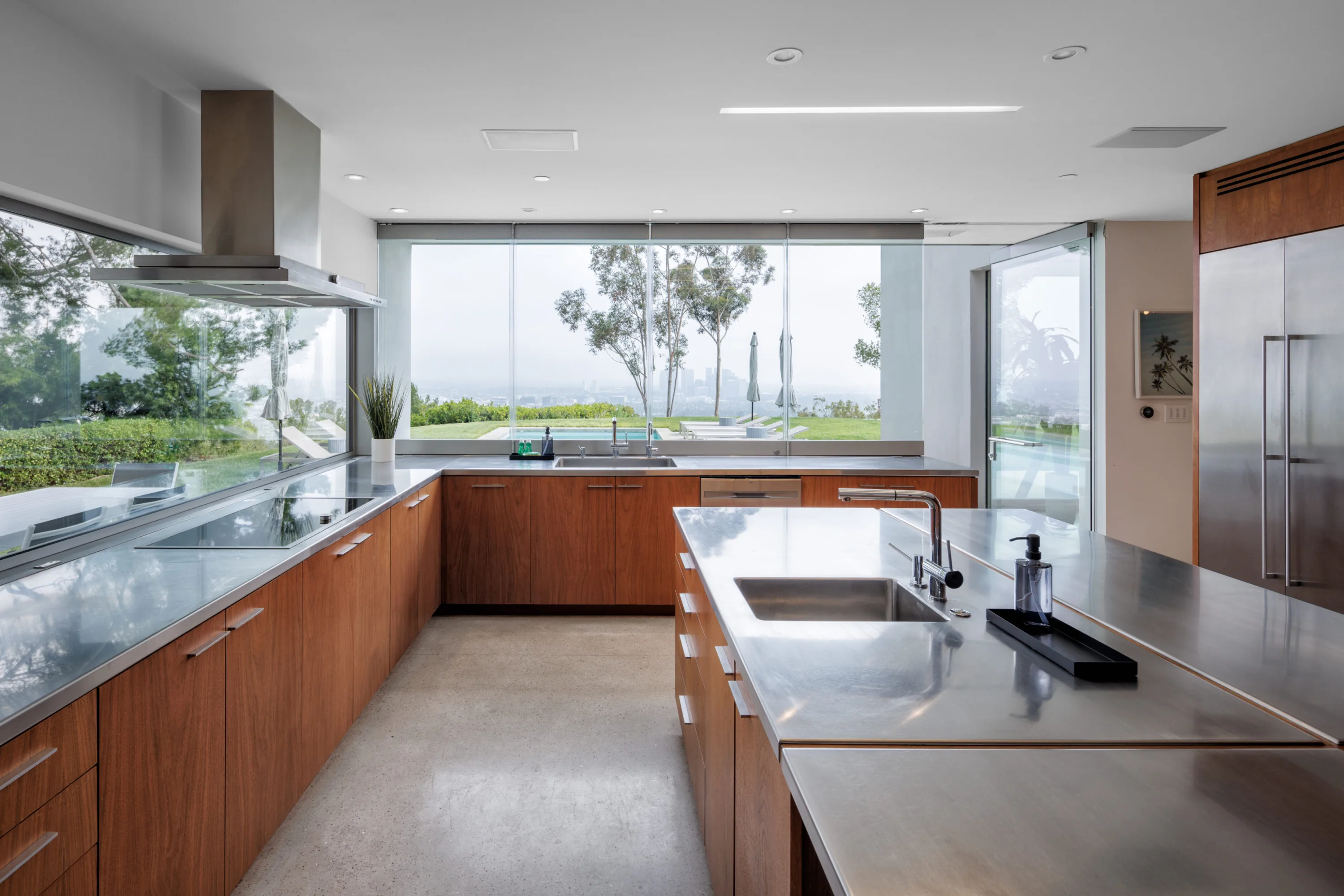 Chef's kitchen in walnut and stainless steel, window over the sink framing the pool, lawn and skyline