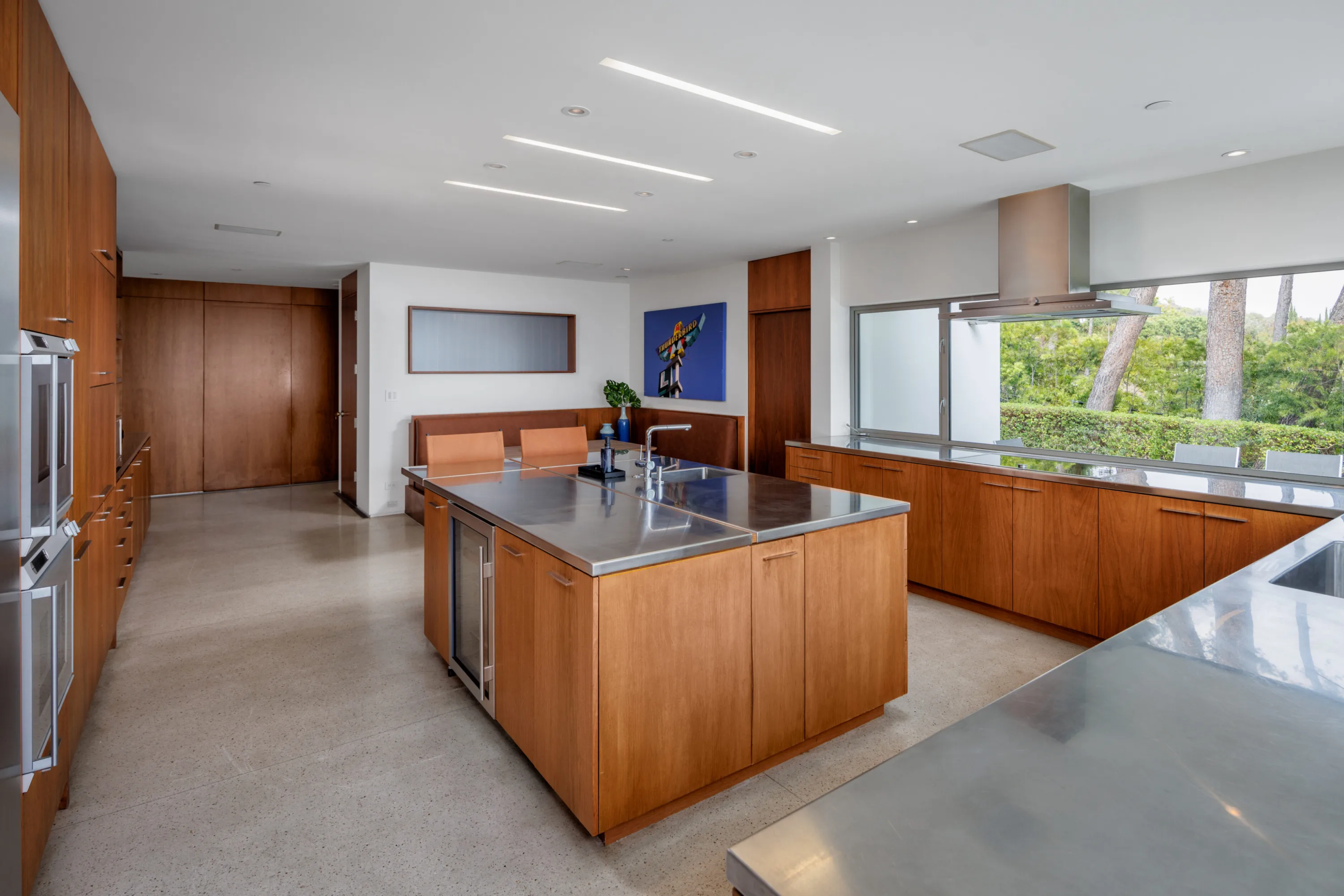 Second view of the kitchen: long stainless island, wall ovens and treetop window above the counter