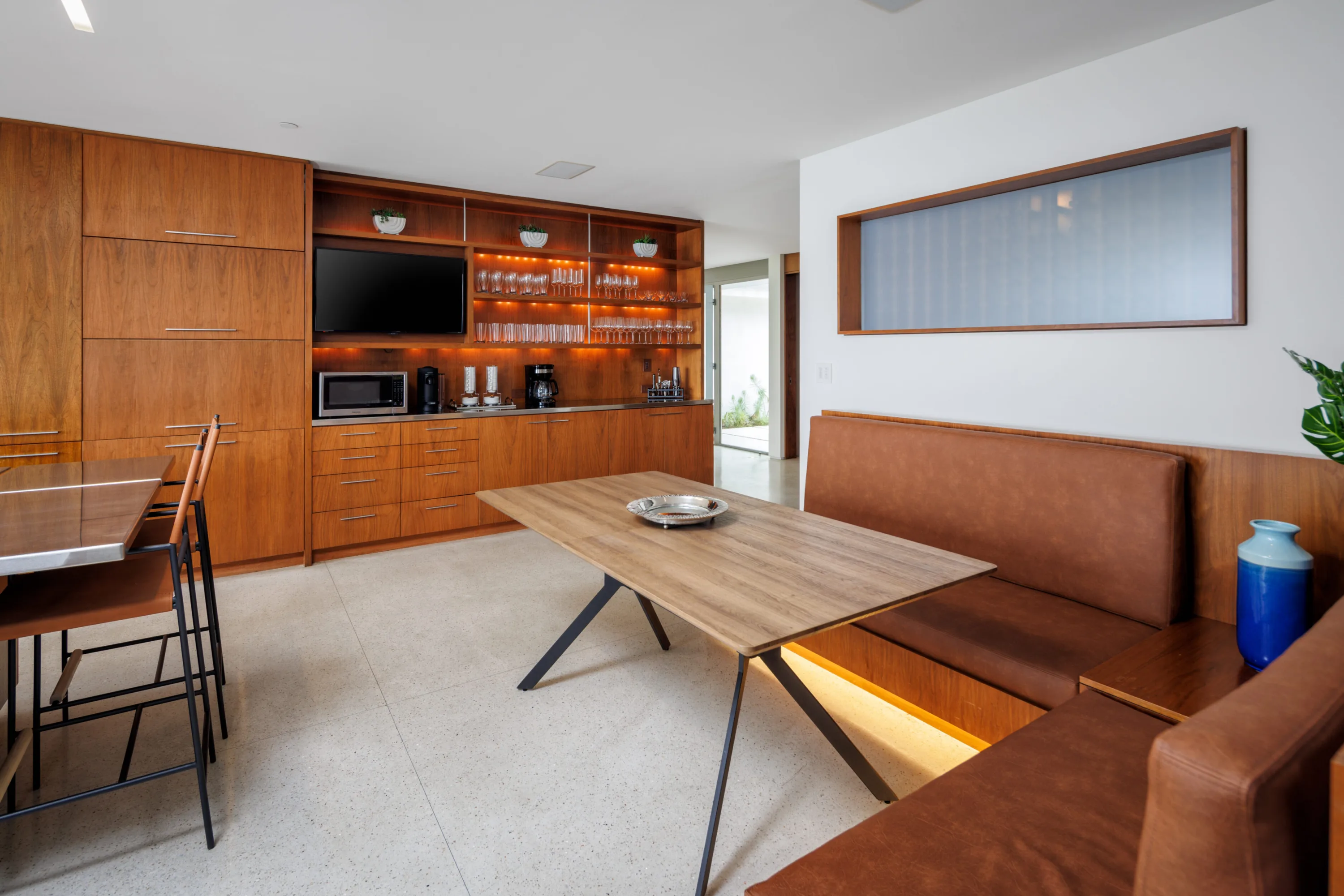 Casual dining nook with leather banquette, oak table and a walnut beverage bar with glassware and TV