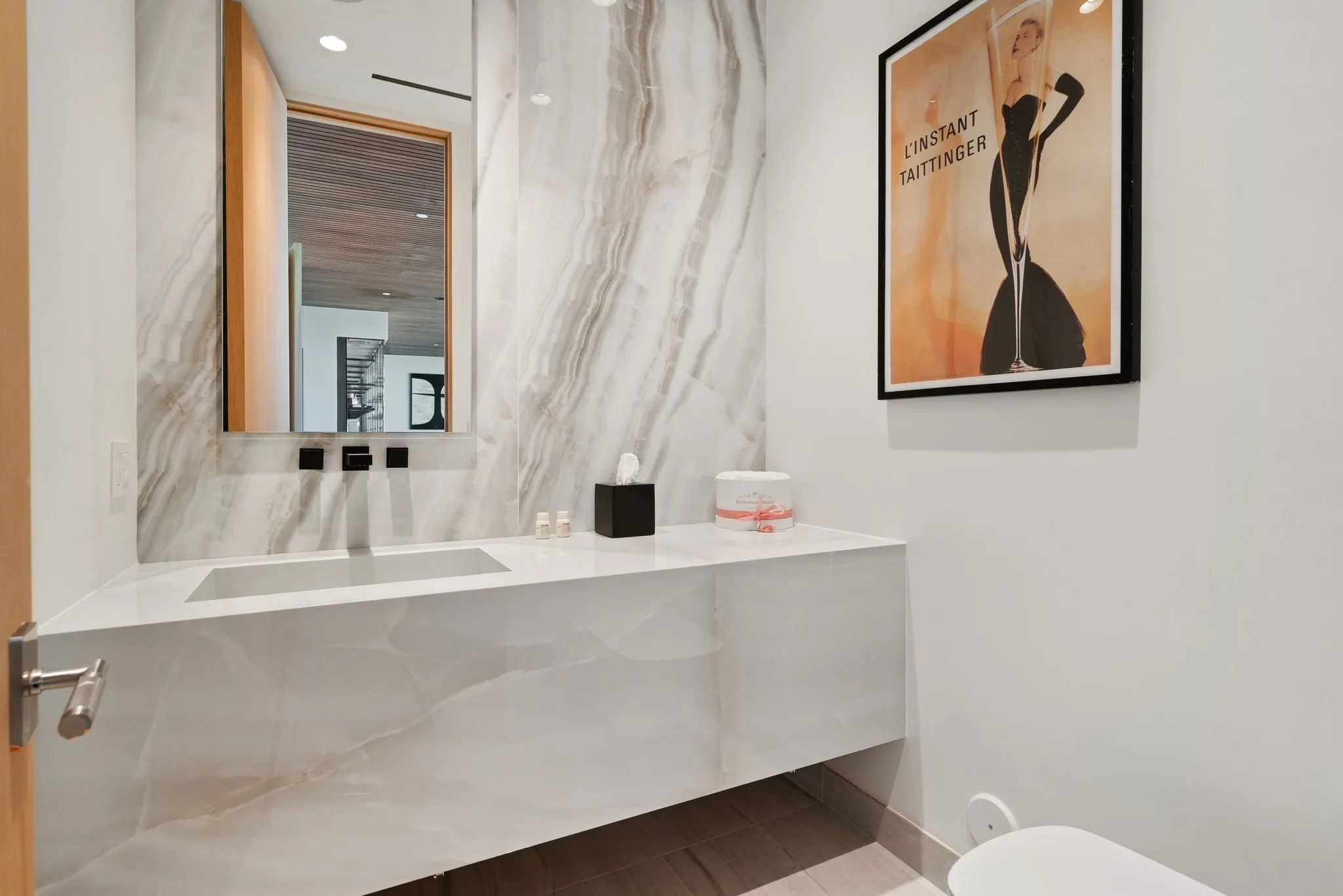 Powder room with floating stone vanity, backlit mirror and framed L'Instant Taittinger poster