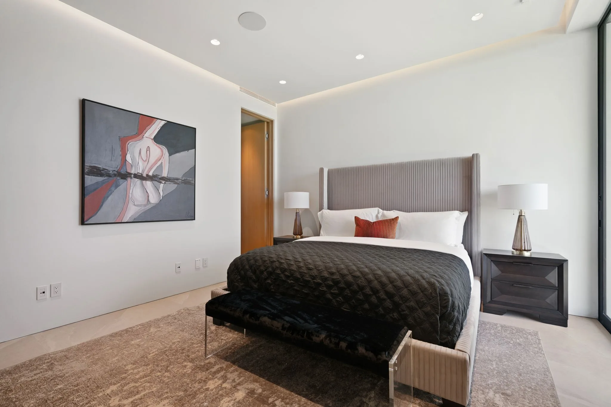 Guest bedroom with tall upholstered headboard, charcoal quilted throw and abstract canvas on a white wall