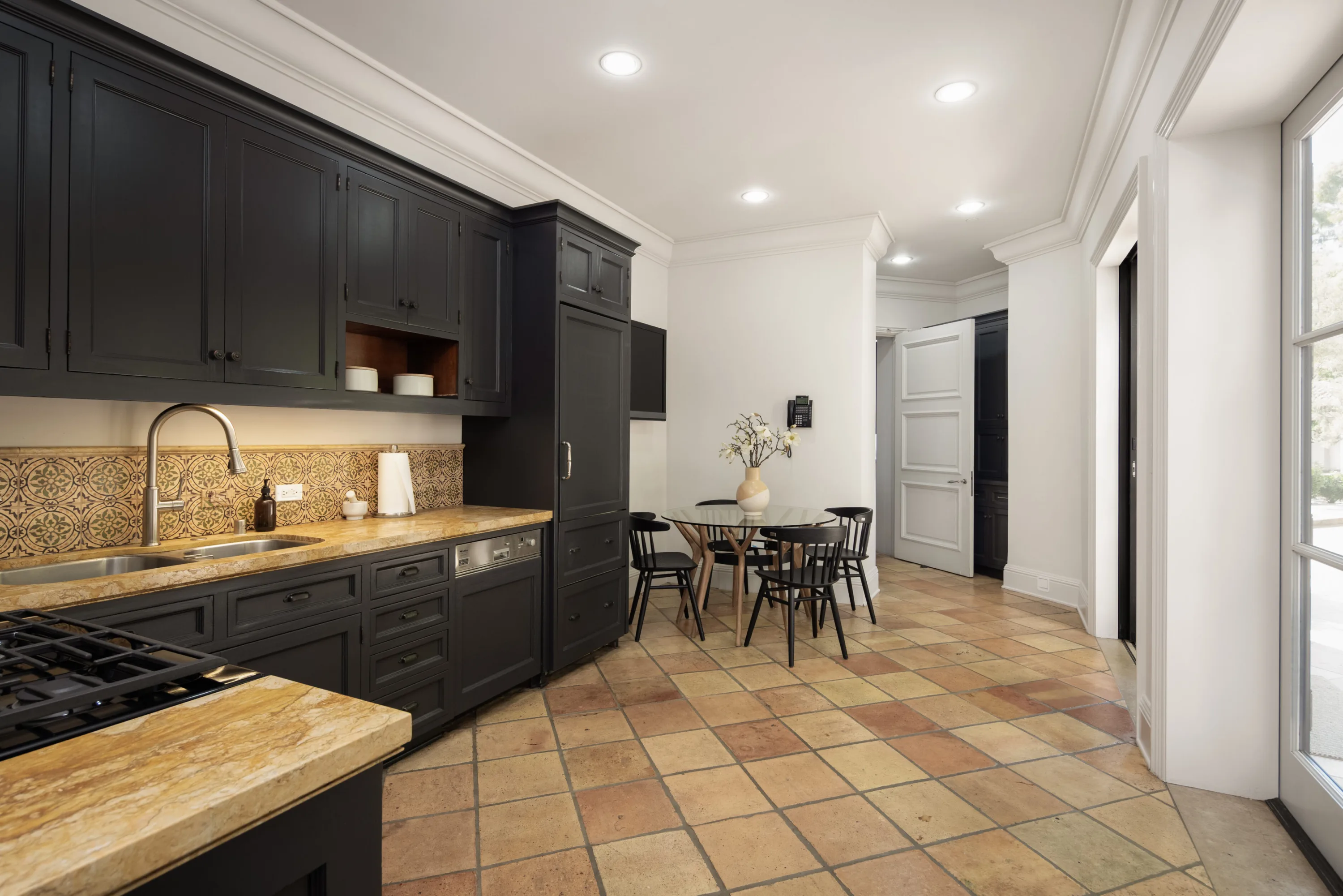 Chef's kitchen in black cabinetry with patterned tile splashback, gas range and round breakfast table for four