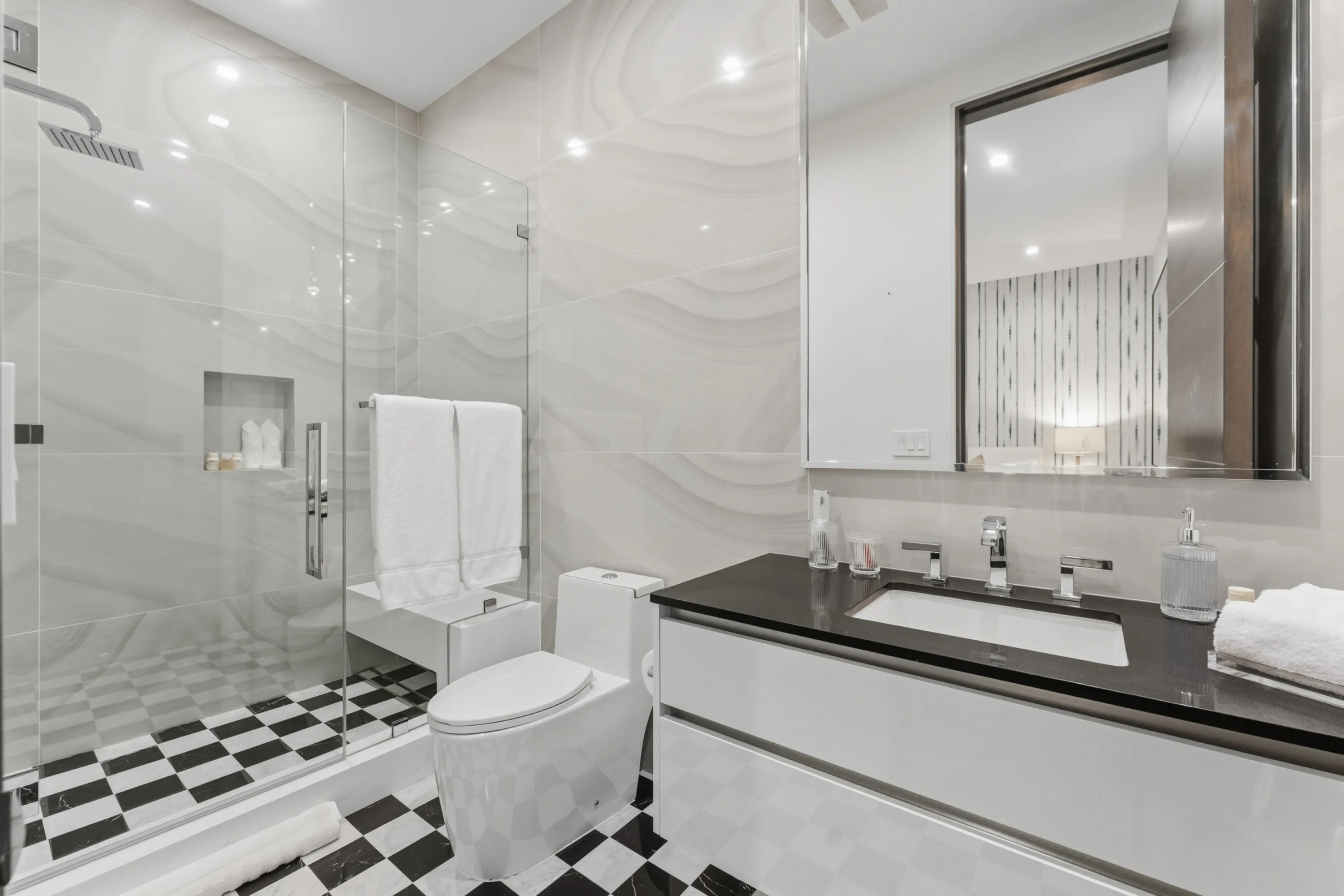 Guest bathroom pairing wave-textured stone walls with a chequerboard marble floor and glass rain shower