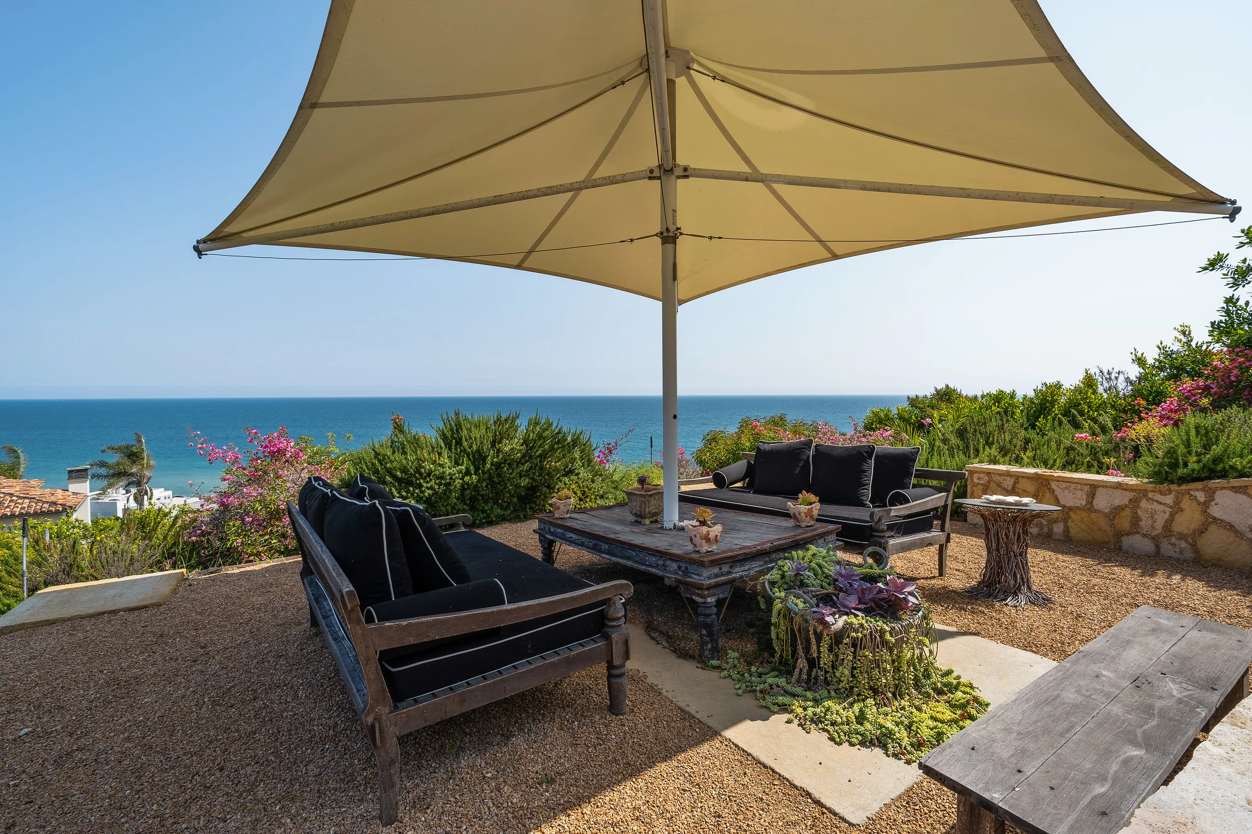 Clifftop lookout with black-cushioned daybeds under a sail canopy, Pacific horizon straight ahead