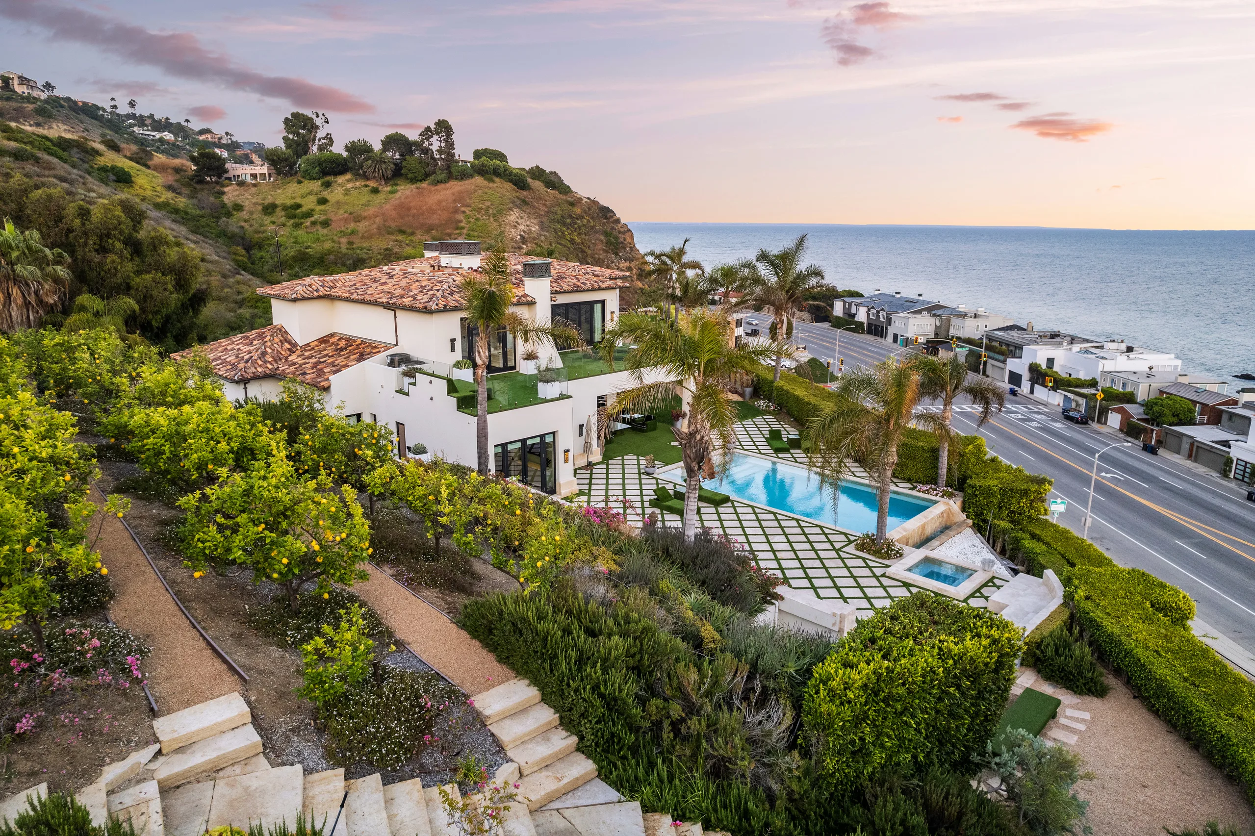 Dusk aerial of the villa, lawn and rectangular pool with the coast highway and ocean beyond