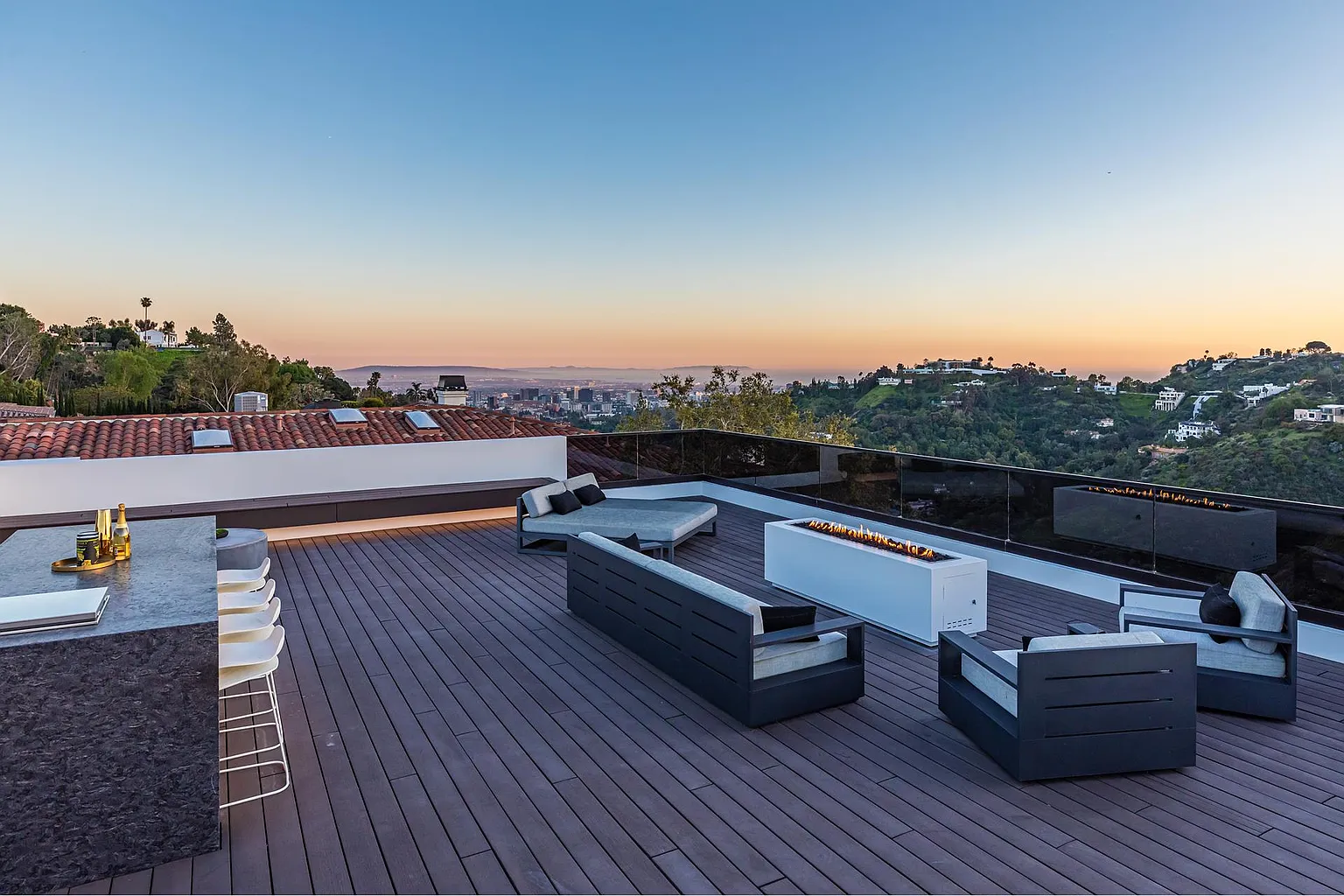 Rooftop terrace at dusk with linear fire table, bar seating and city lights spreading to the horizon