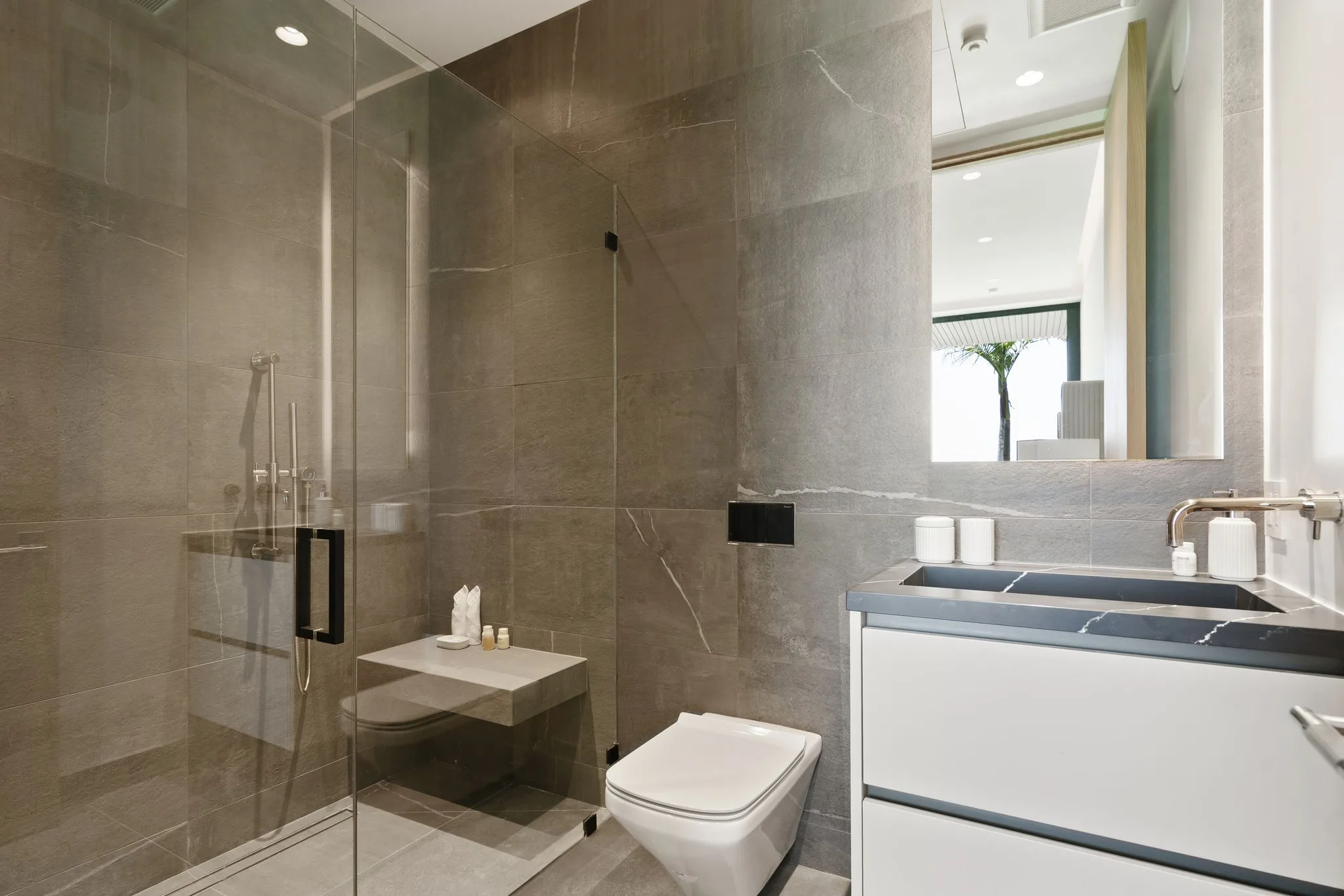 Ensuite shower room clad in grey stone with walk-in glass shower and floating white vanity