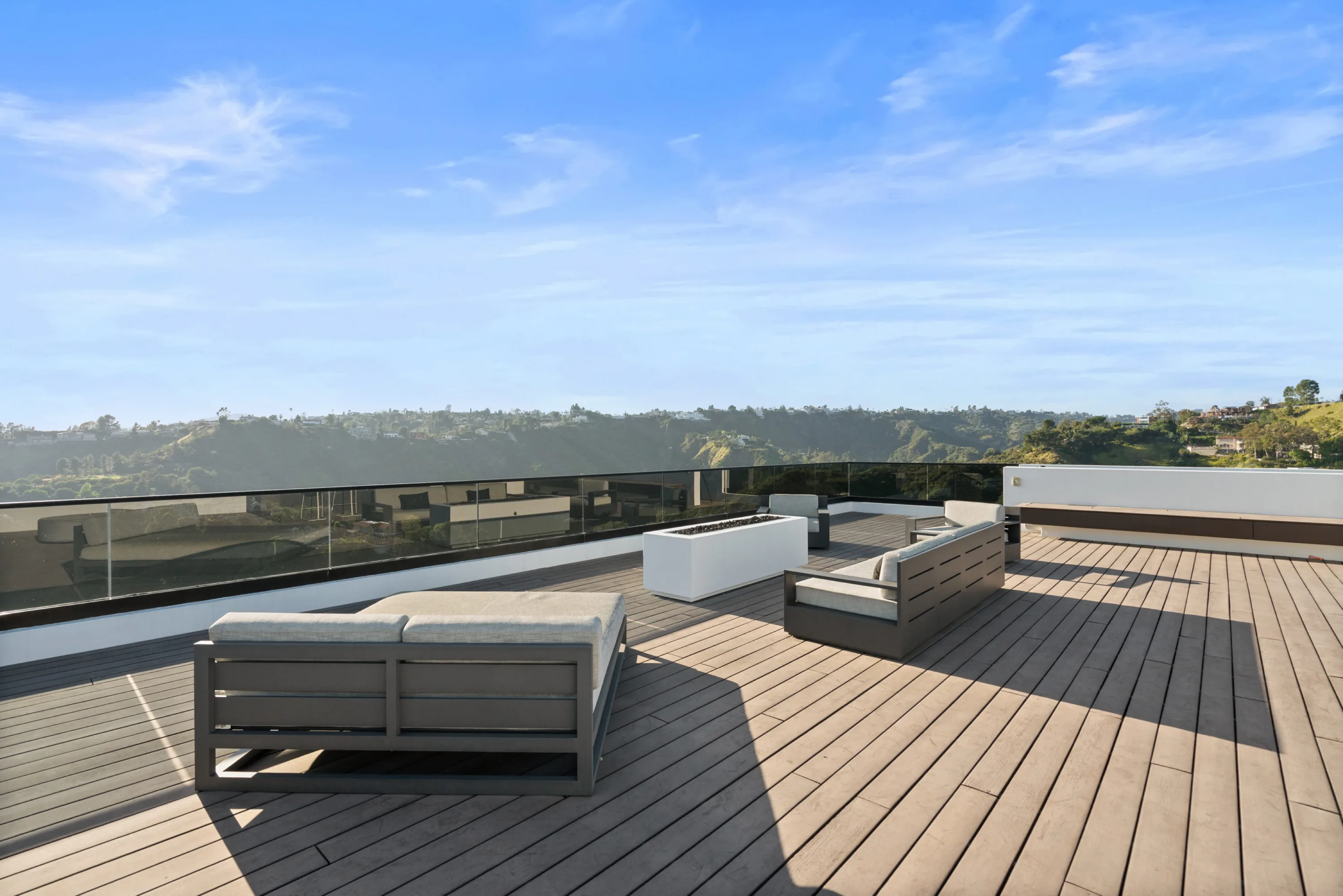 Sun-washed roof deck with lounge seating and glass balustrade open to the Bel Air canyon ridgeline