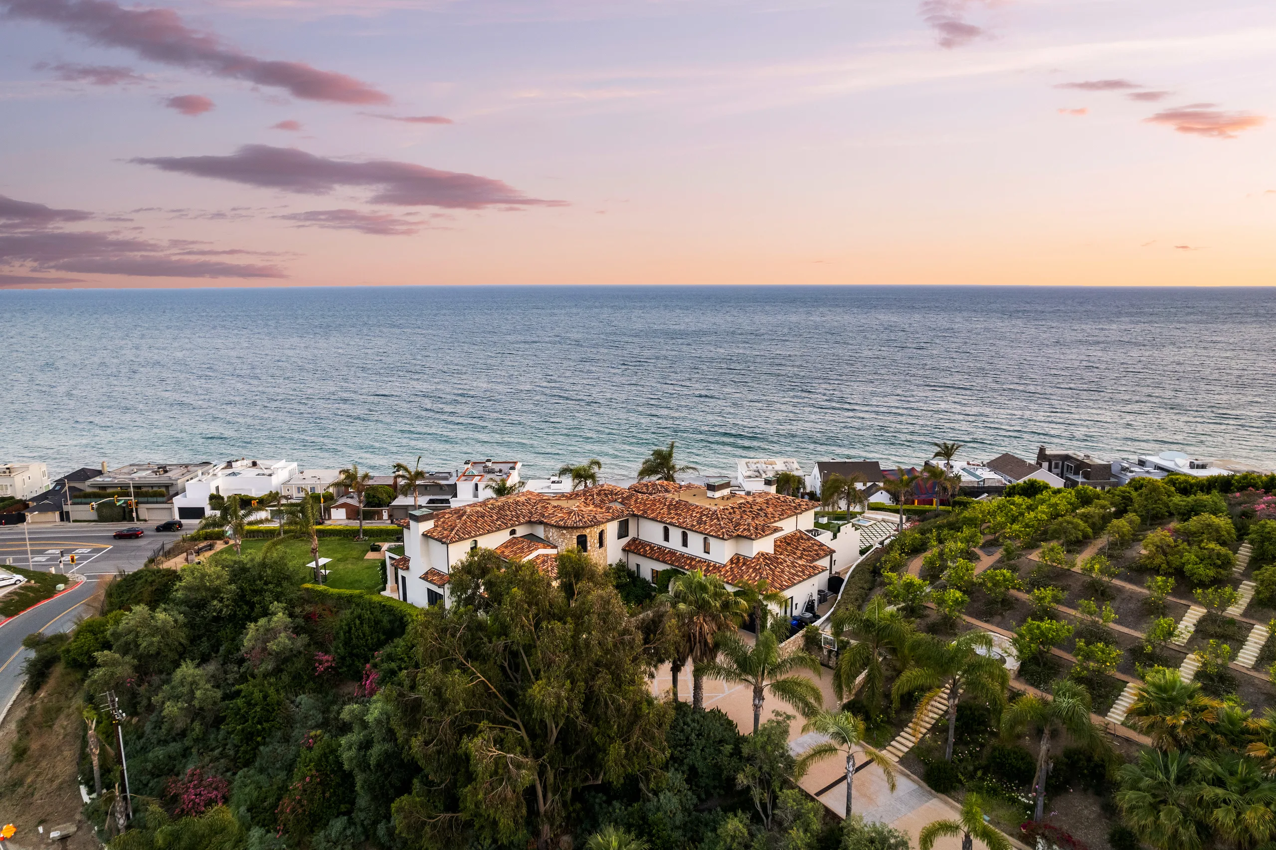 Drone shot of the terracotta-roofed estate set among palms and citrus terraces facing the open sea at dusk