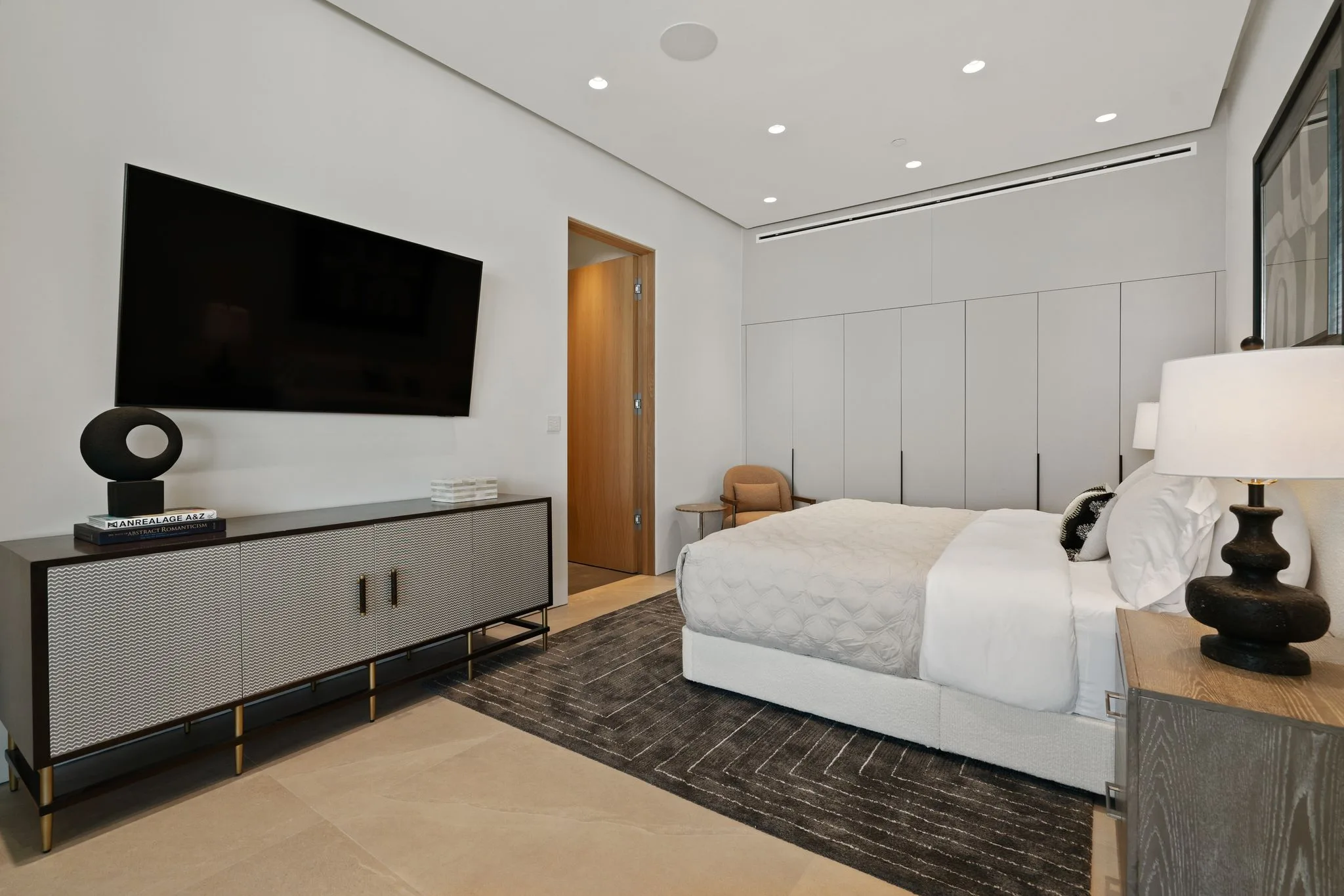Bedroom with wall-mounted television, patterned credenza and built-in wardrobes behind the bed