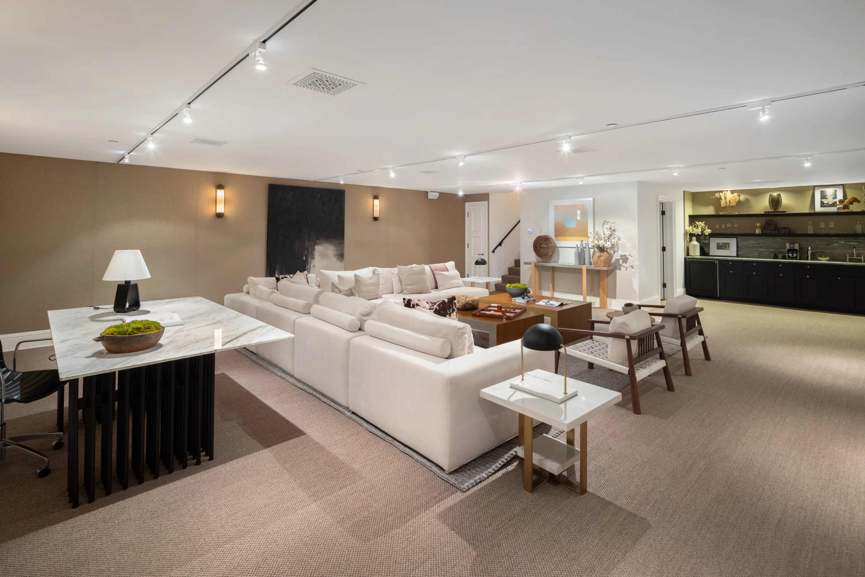 Lower-level lounge with long sectional sofa, games table and wet bar under track lighting