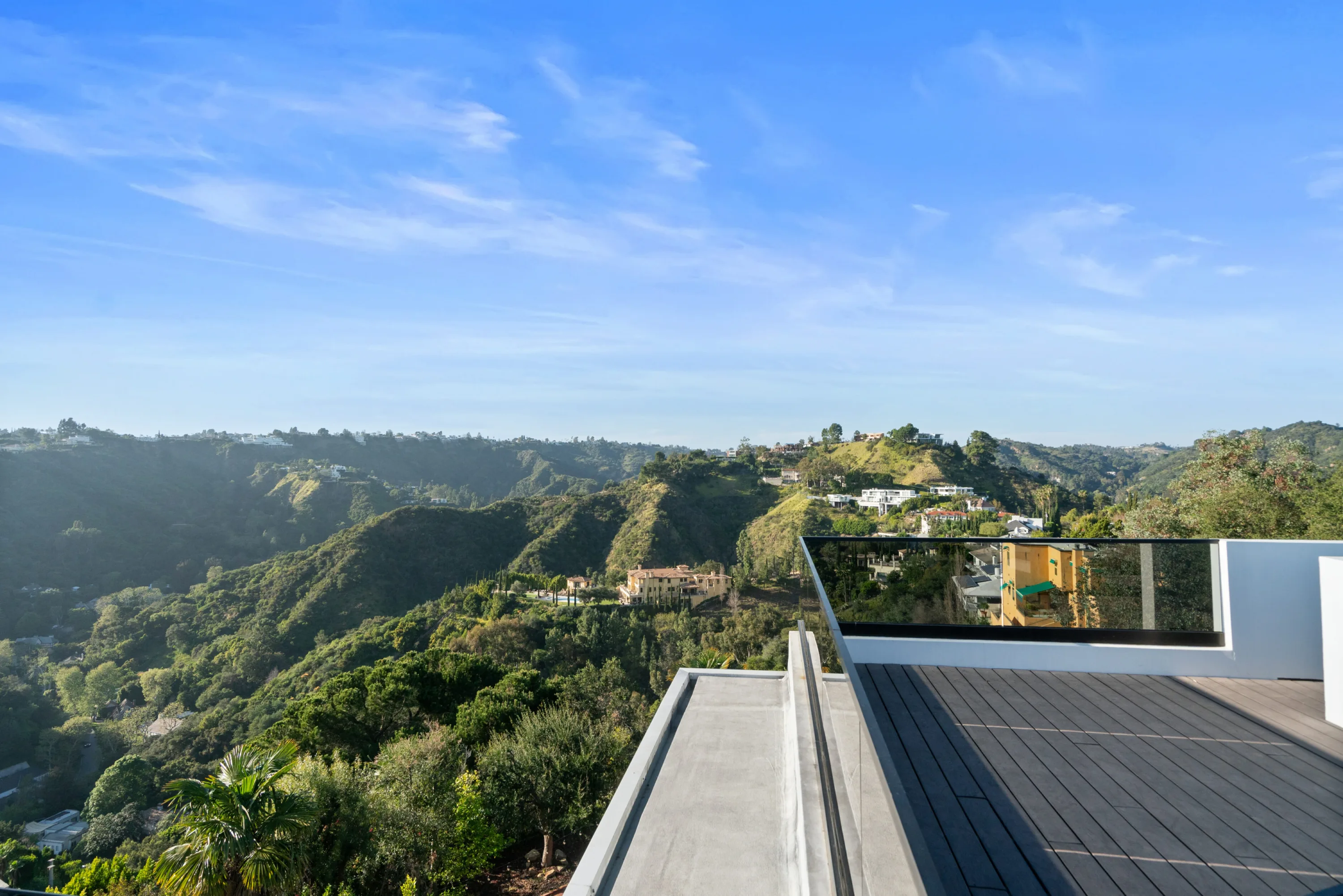 Canyon panorama of wooded hillsides and hilltop houses seen past the deck's mirrored glass rail