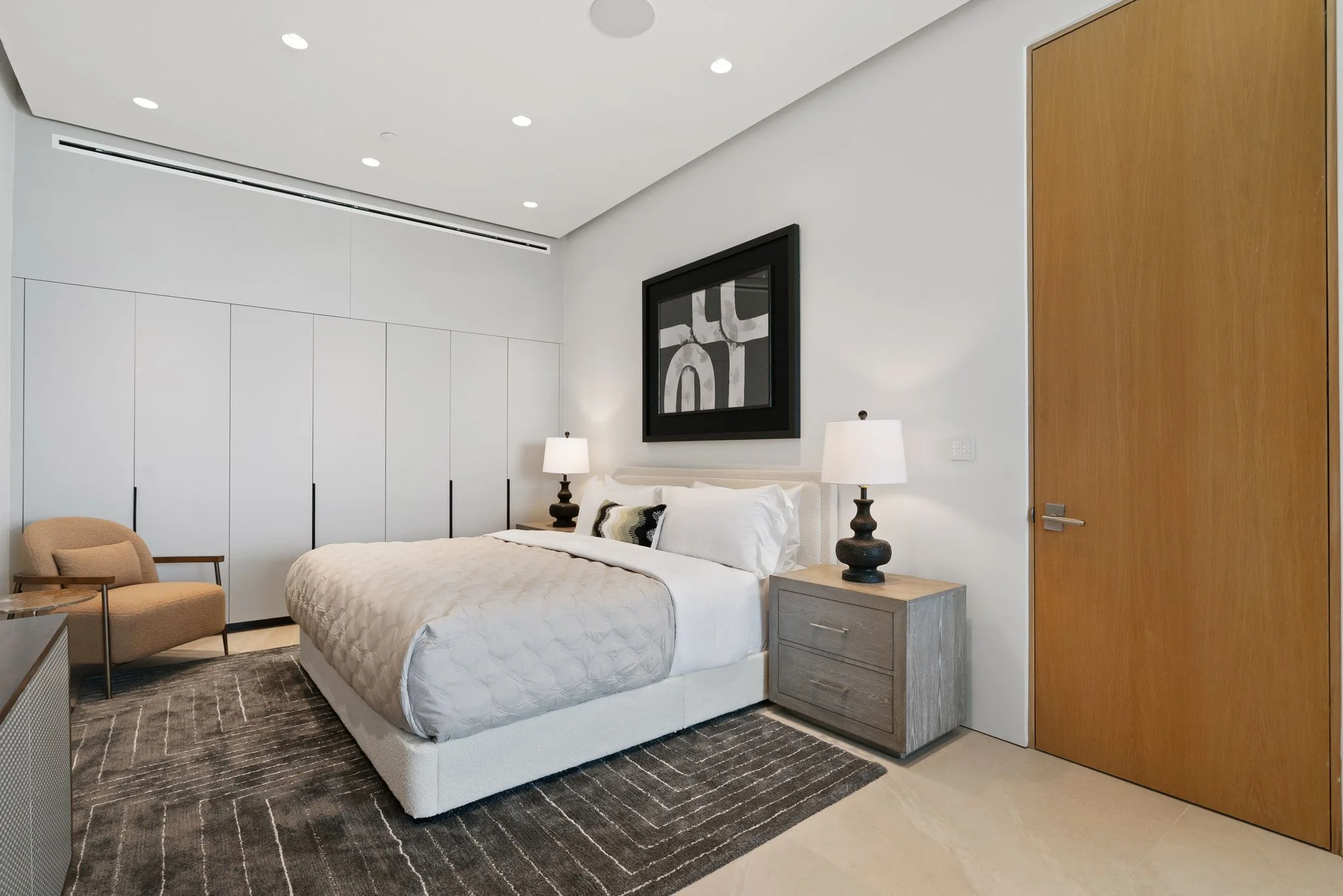 Crisp white guest room with bouclé bed, paired lamps, armchair and a run of full-height closets