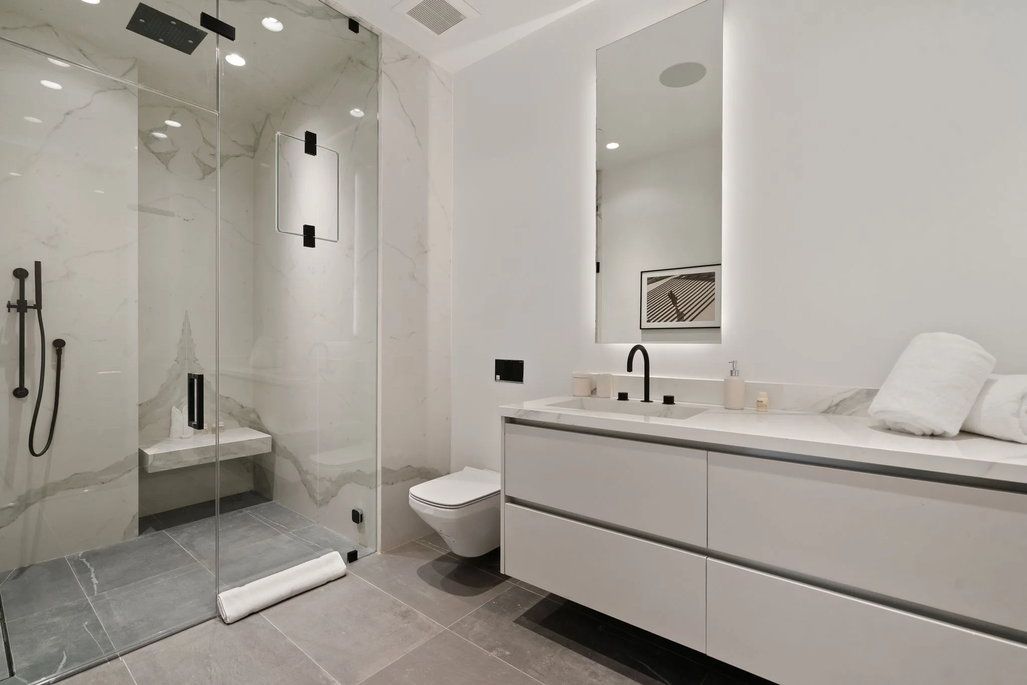 Marble-lined bathroom with walk-in rain shower, built-in bench and long backlit mirror over the vanity
