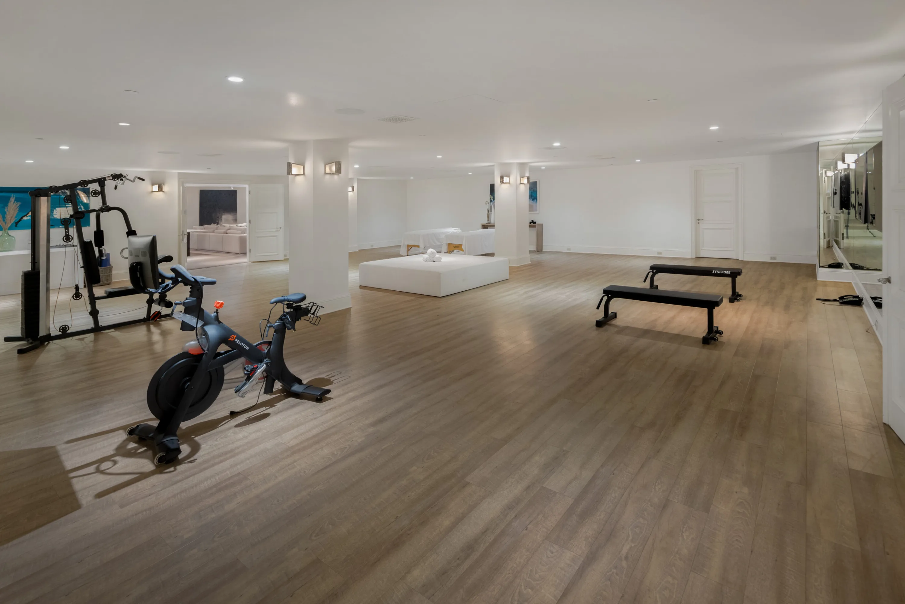 Spacious wood-floored gym with spin bike, multi-station weight machine, benches and mirrored wall