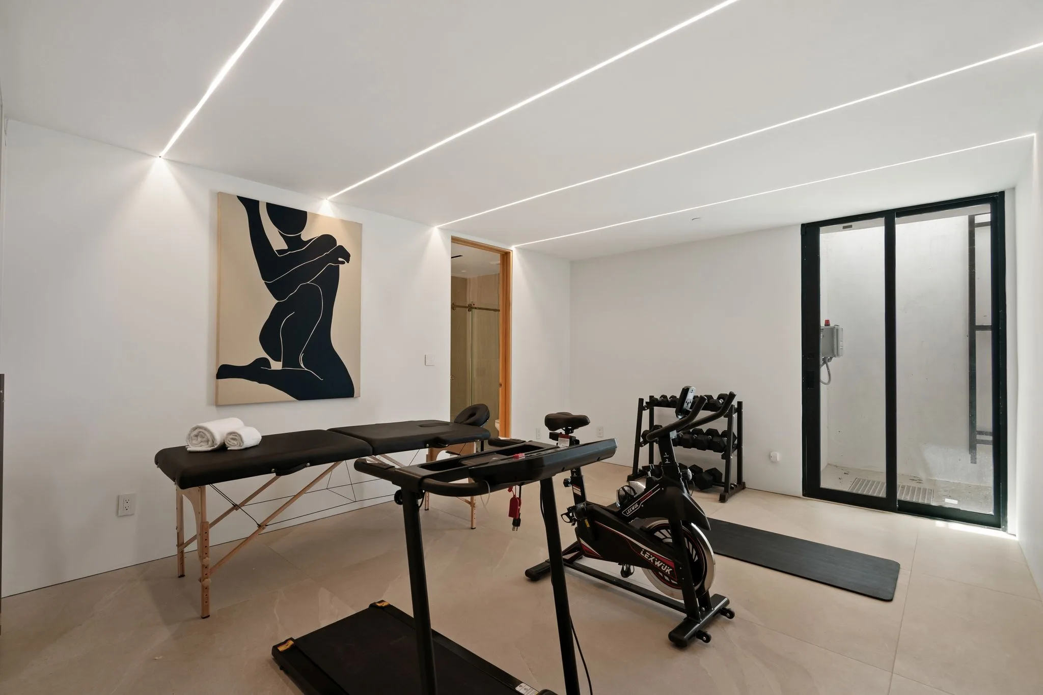 Private gym with treadmill, spin bike, dumbbell rack, massage table and figurative artwork