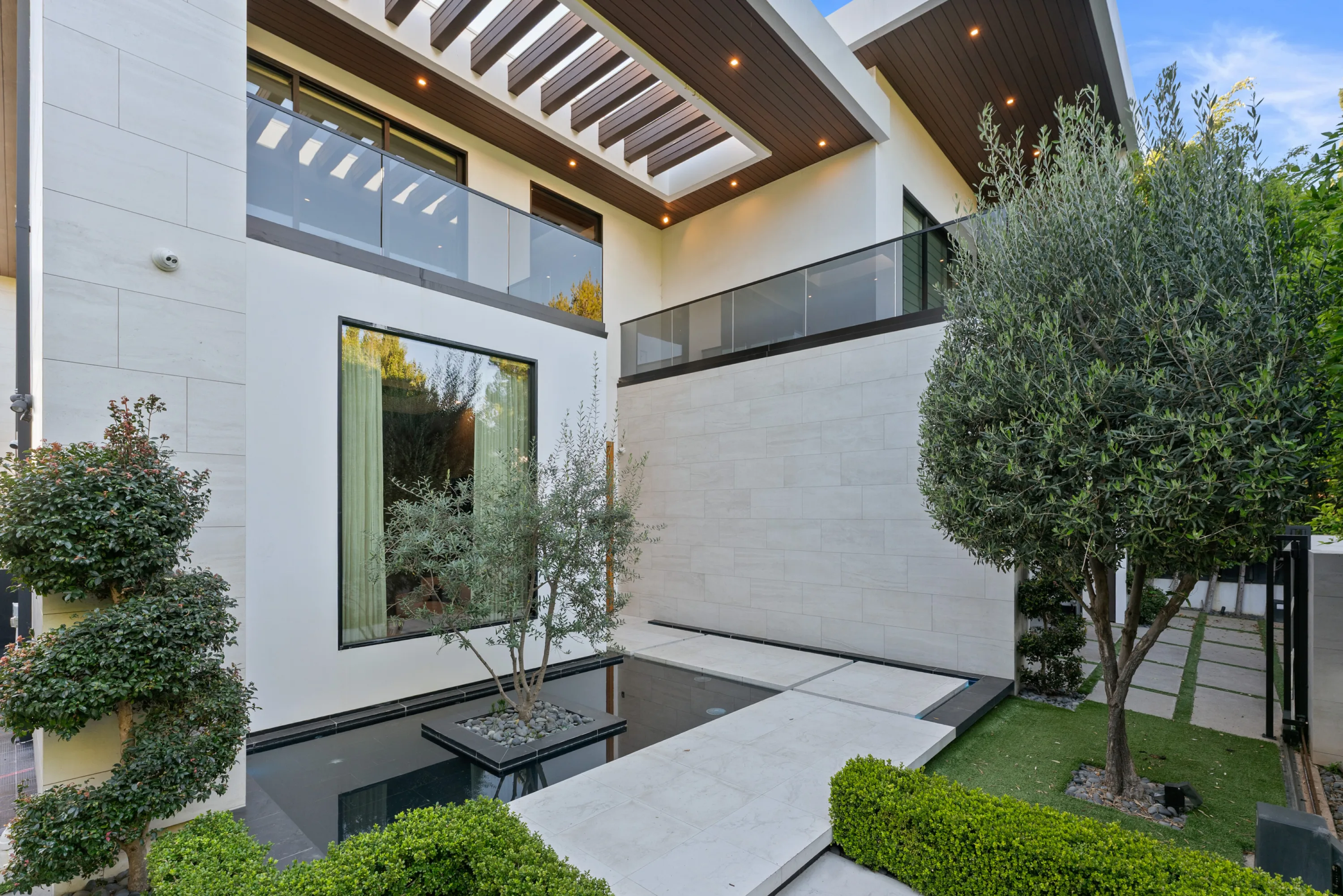 Slatted timber soffit and glass balcony above the black reflecting pond and stepping-stone path at the entrance