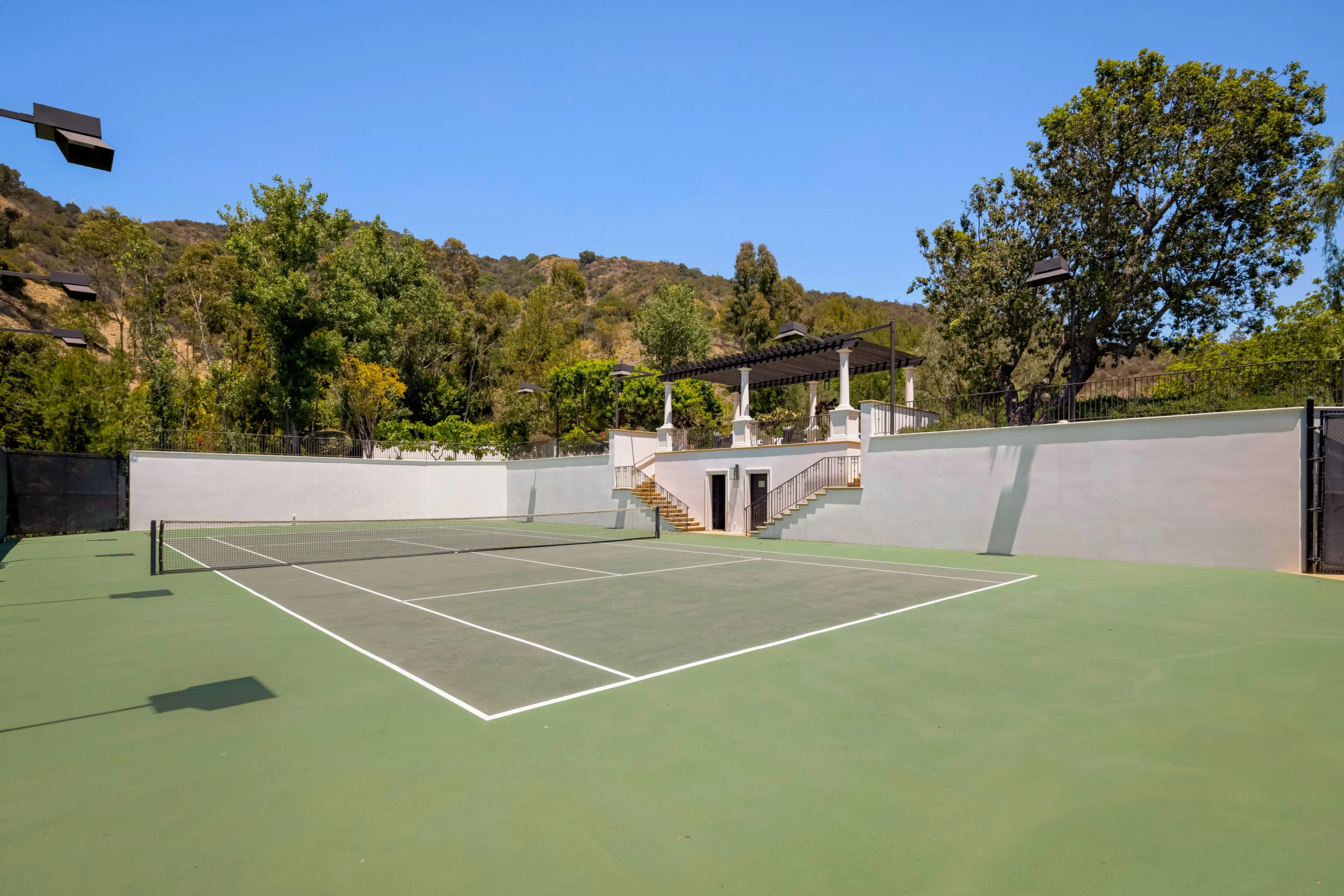 Private tennis court set below the hillside, with floodlights and a vine-covered pergola above the steps