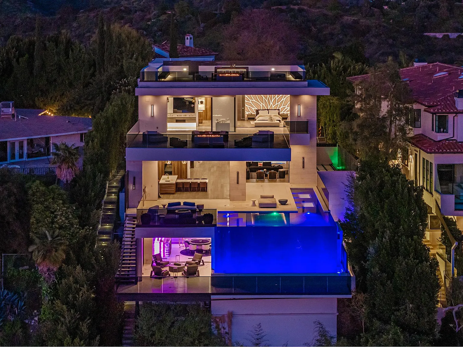 Estate lit at twilight, three storeys of open glass above the illuminated blue infinity pool