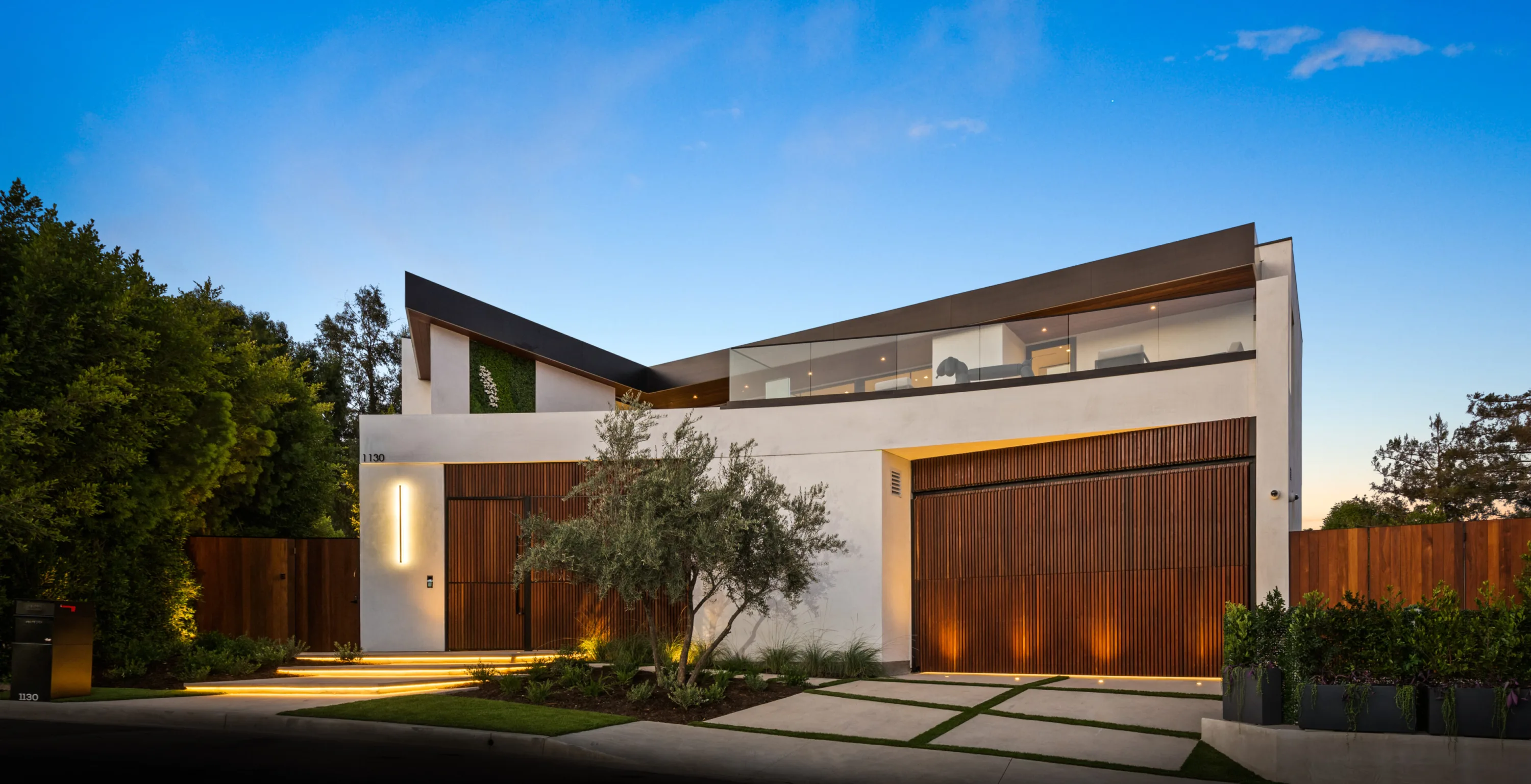 Street frontage at dusk with slatted timber gates and an olive tree beside the entry