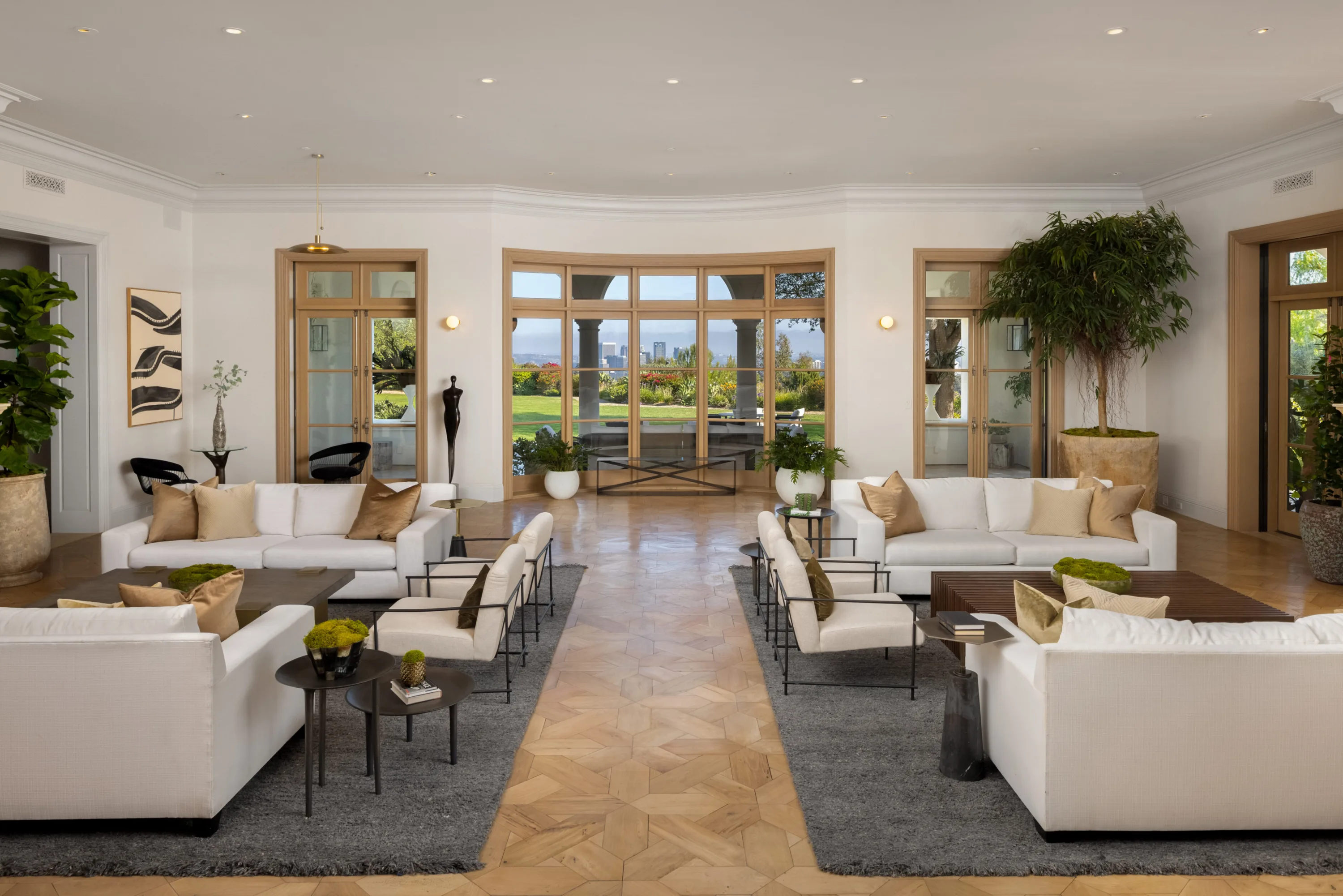 Formal living room with twin white sofa groupings and curved window wall framing lawn and downtown skyline