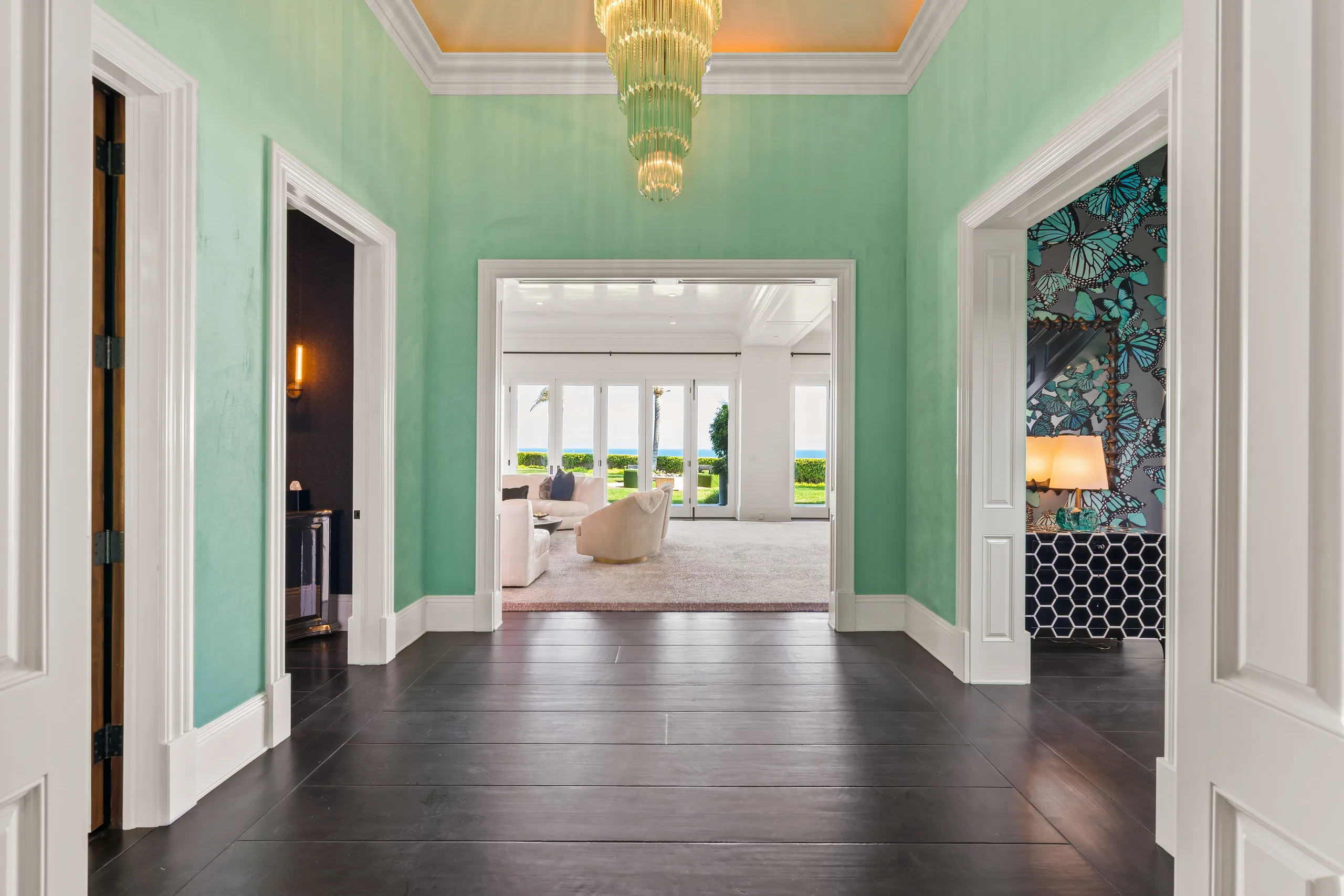 Entry hall in mint lacquer with tiered chandelier, sightline through the living room to the sea