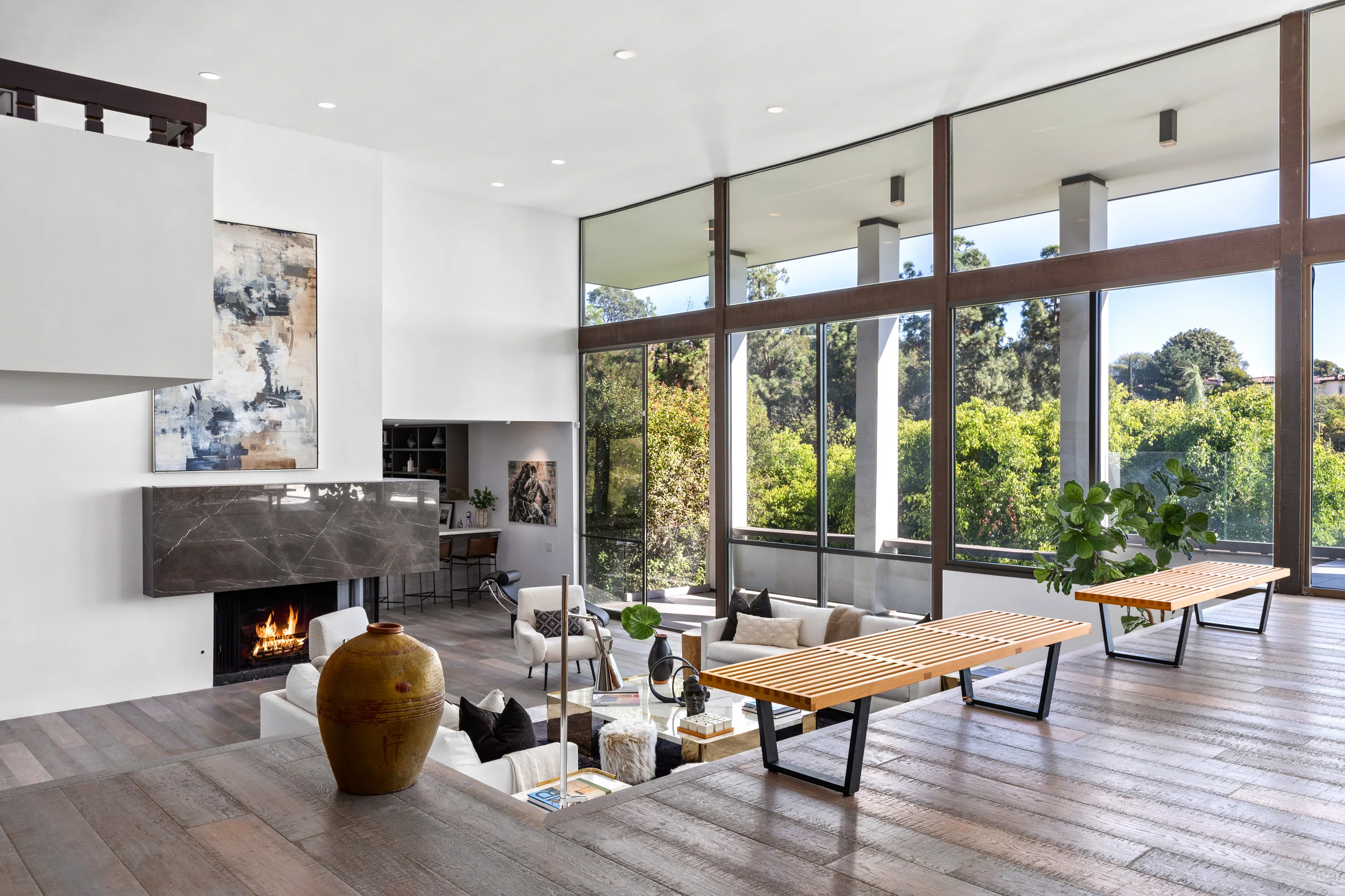 Double-height living room with lit fireplace, stone surround and a wall of clerestory windows onto greenery