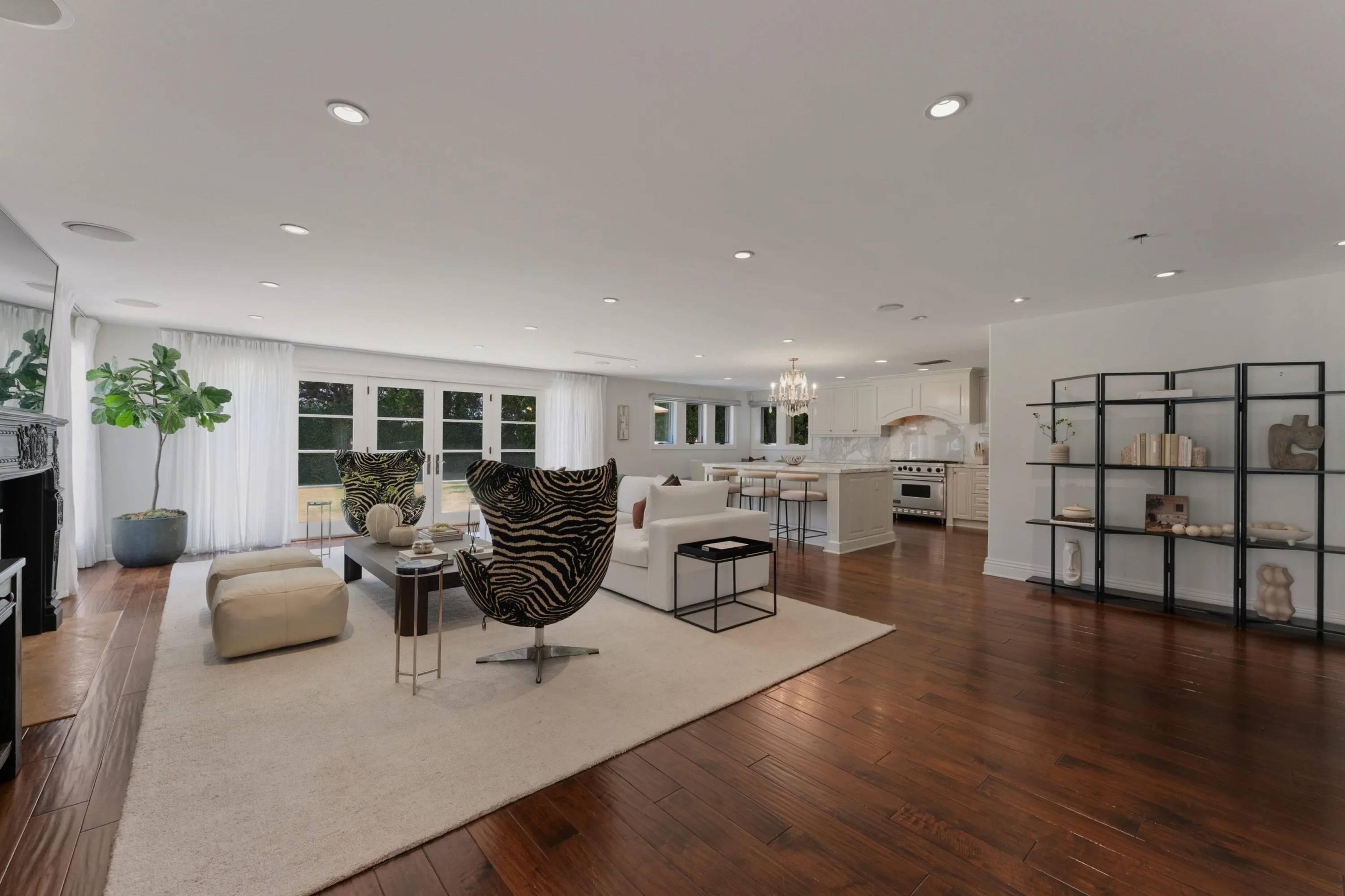 Open-plan great room flowing past zebra-print chairs to the white kitchen and island bar stools