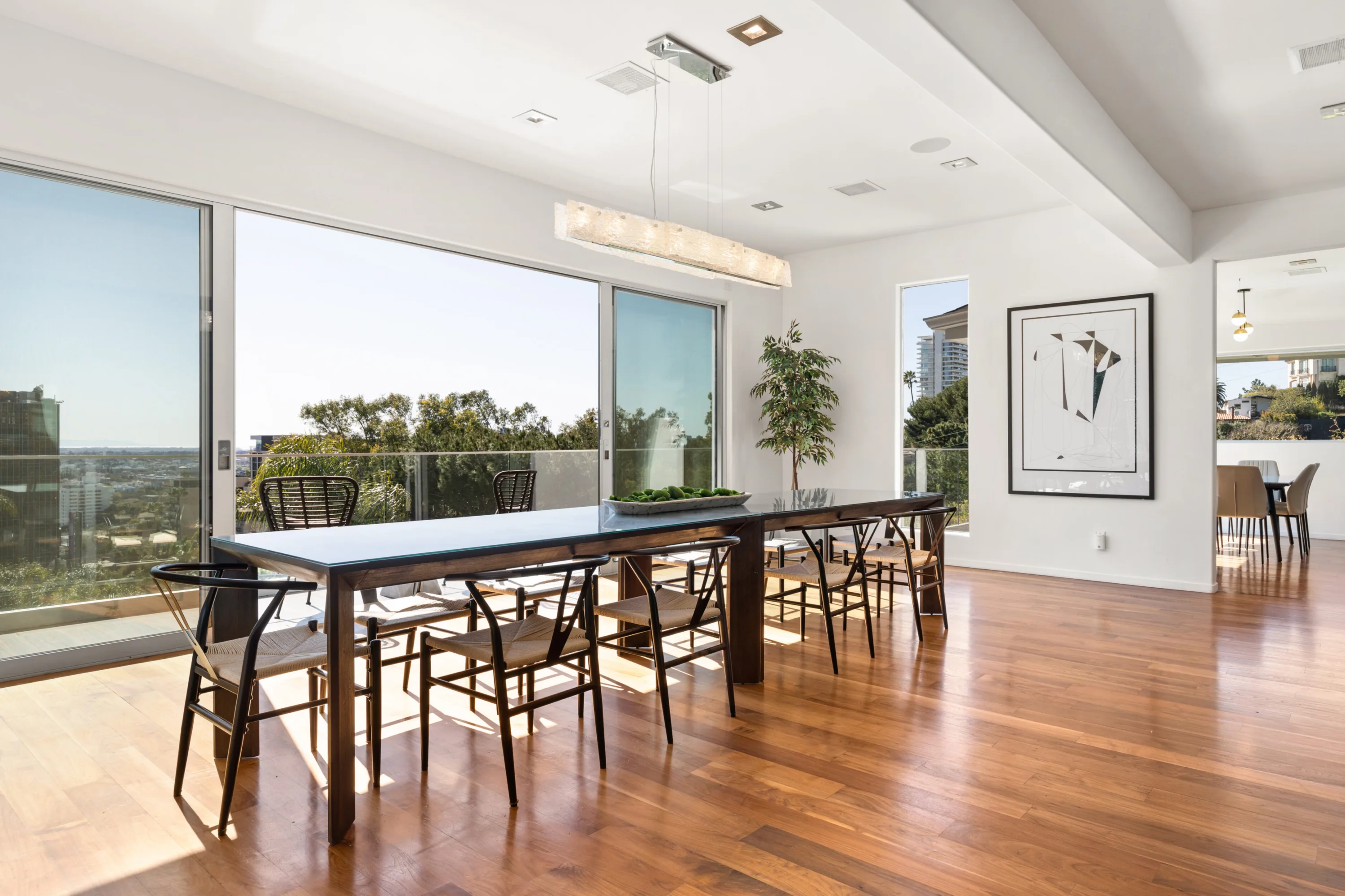 Dining room on polished hardwood, sliding doors open to a glass-railed terrace above the hills