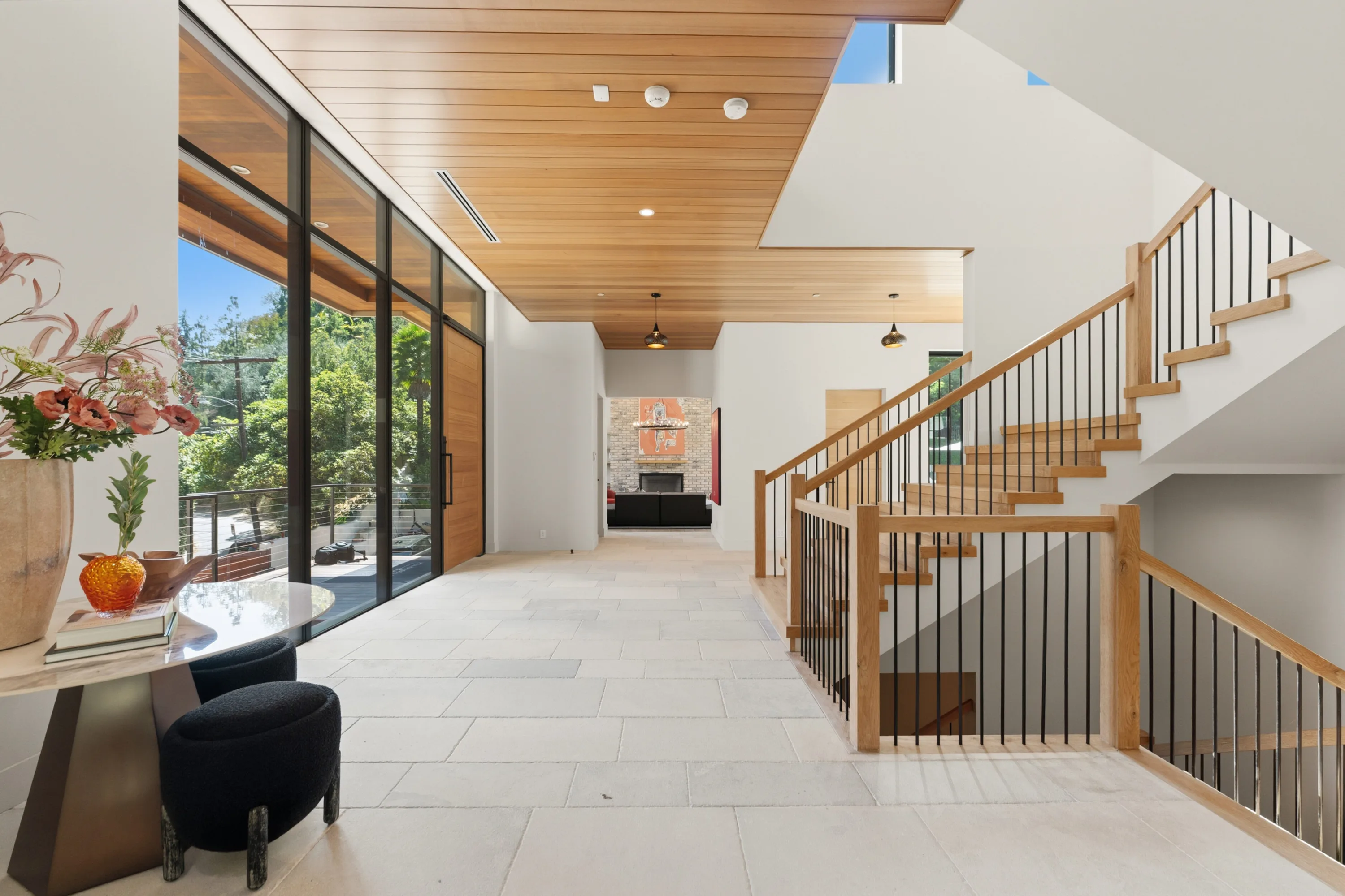 Entry hall with wood-slat ceiling, oak staircase and floor-to-ceiling glass framing greenery beyond