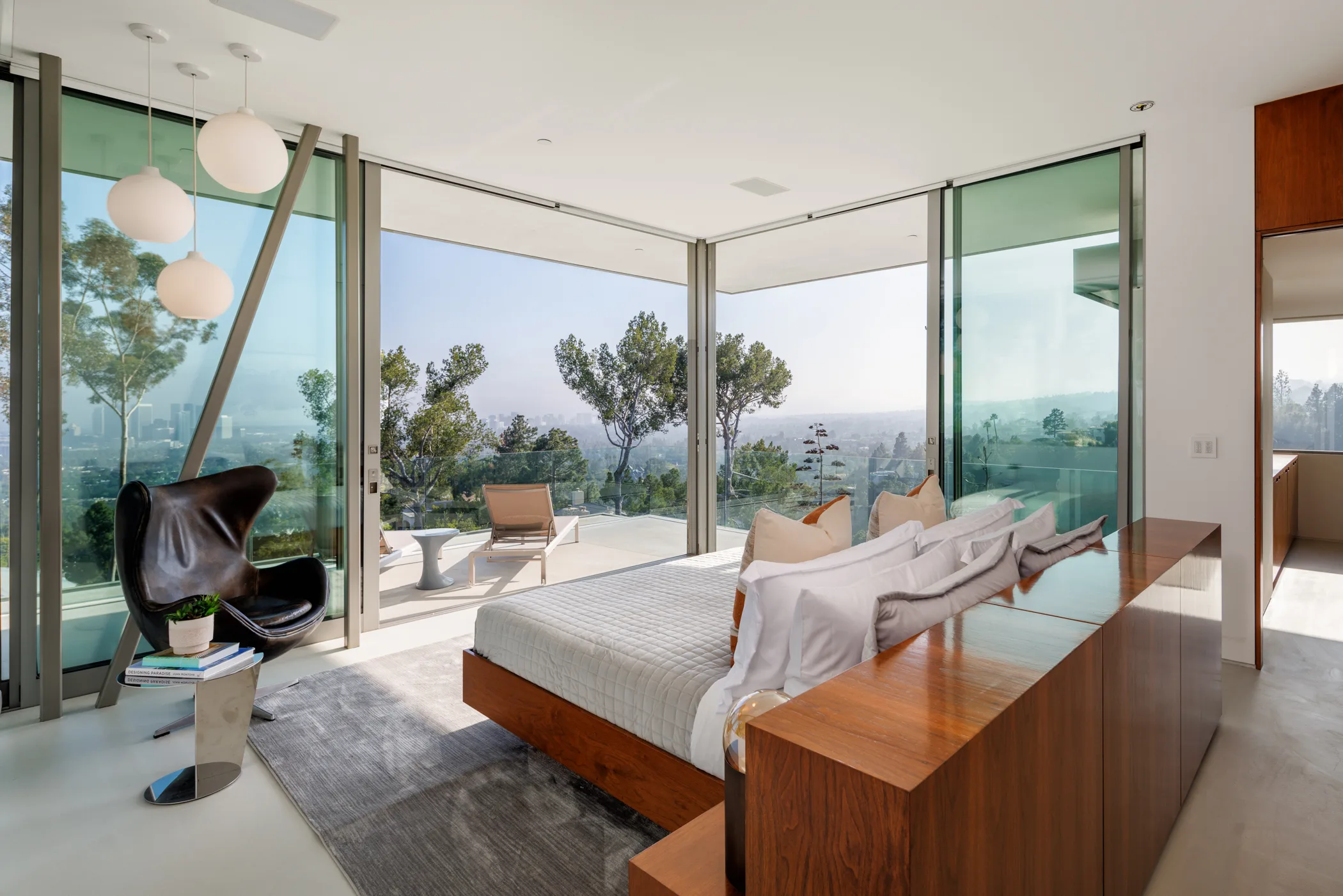 Primary suite wrapped in glass, bed facing a private terrace with lounger and hillside city panorama
