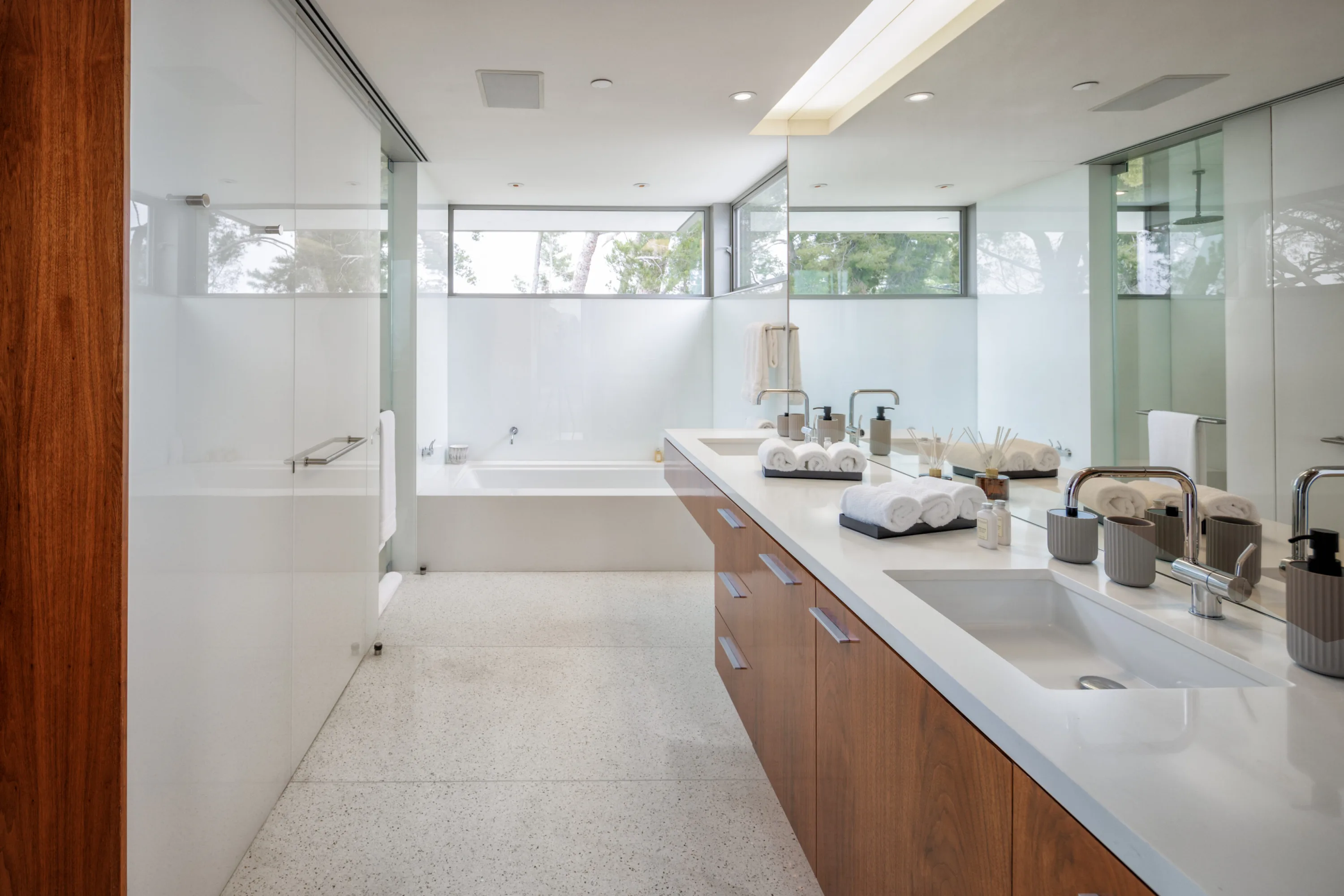 Primary bath with long twin-sink vanity, soaking tub, walk-in shower and clerestory windows to the trees