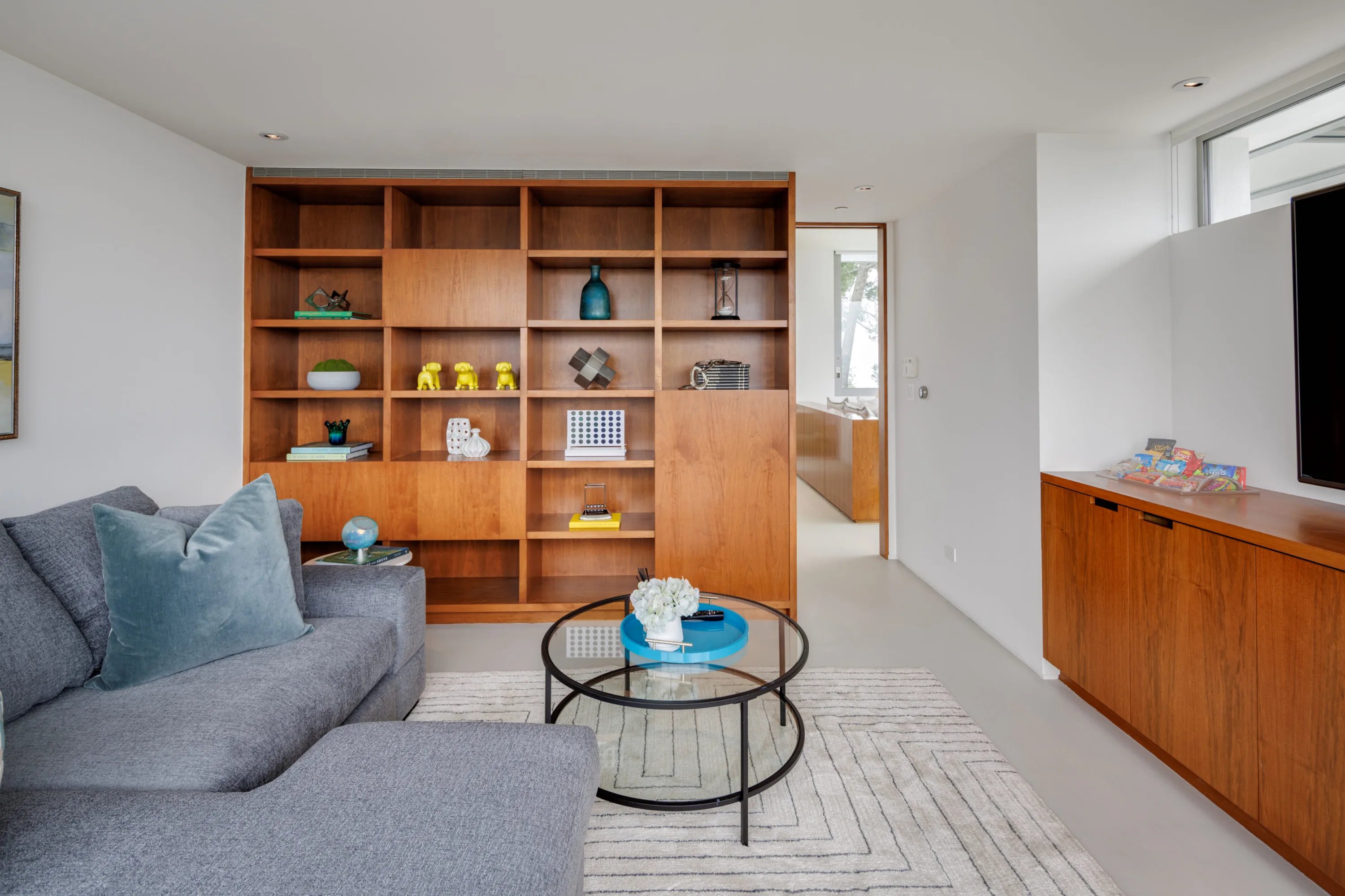 Upstairs den with grey sectional, built-in walnut bookshelves and wall-mounted TV above a credenza