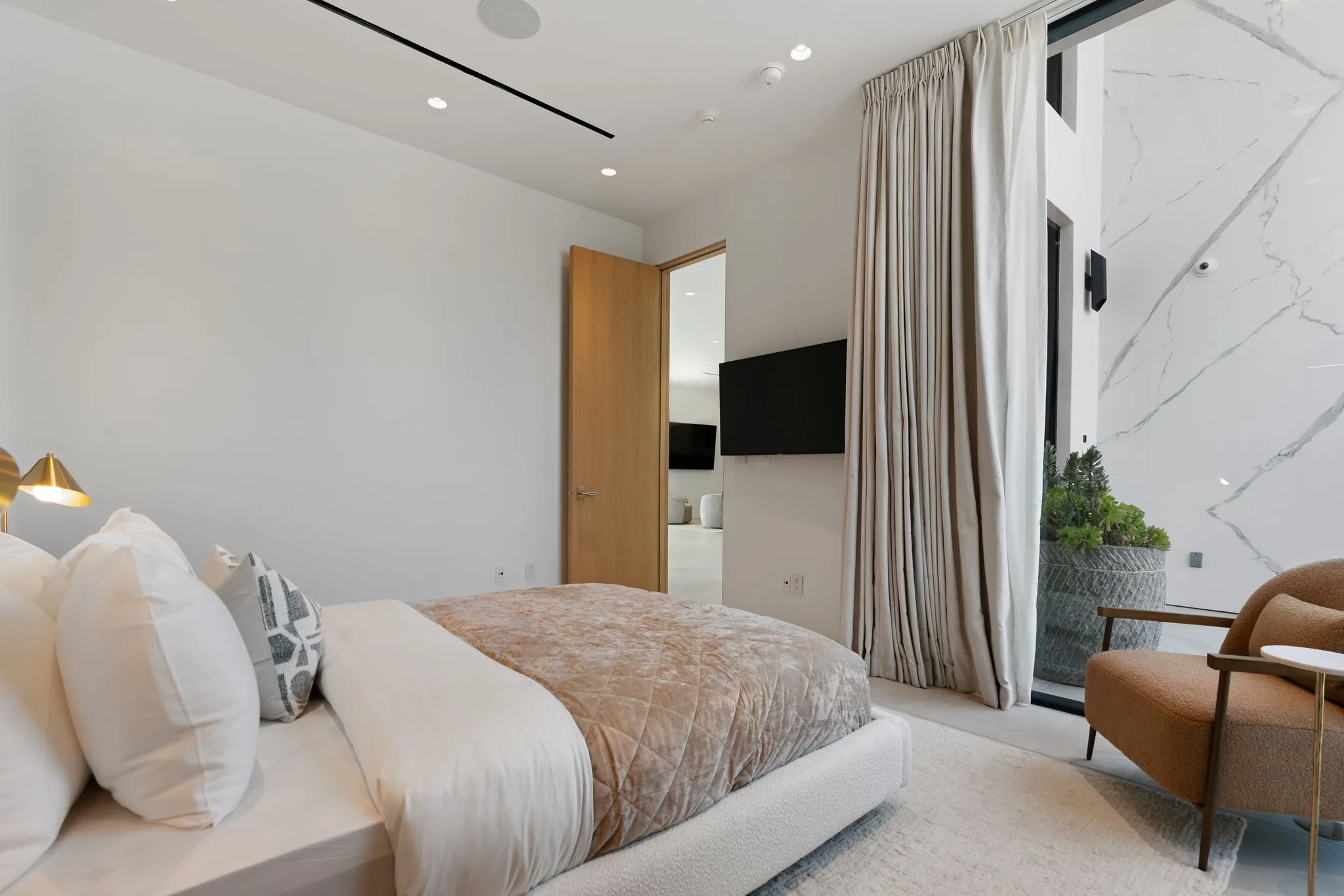 Soft-toned bedroom with velvet coverlet, curtained glass wall and a marble-clad light well outside