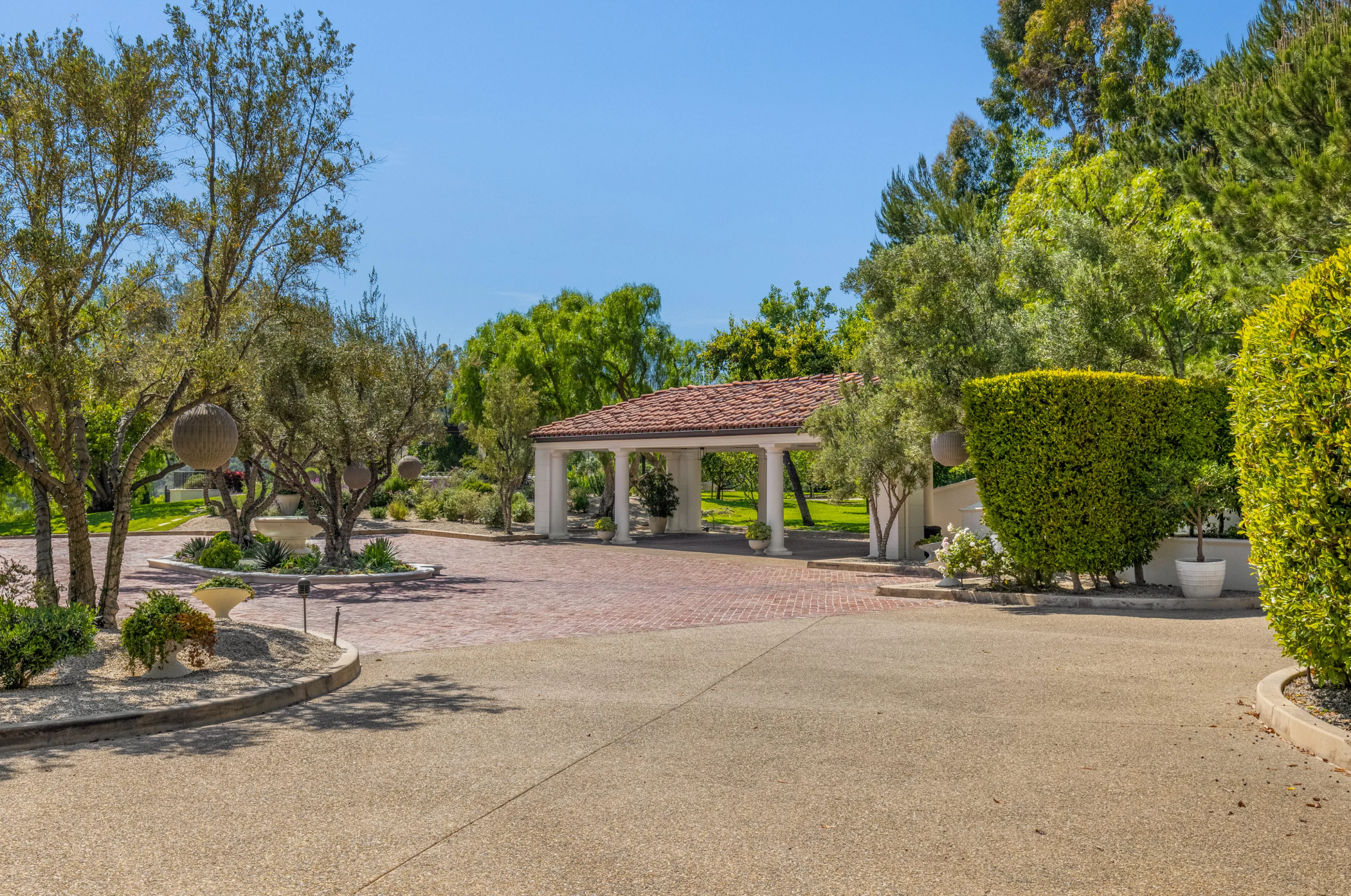 Brick motor court and colonnaded porte-cochère framed by olive trees and clipped hedges