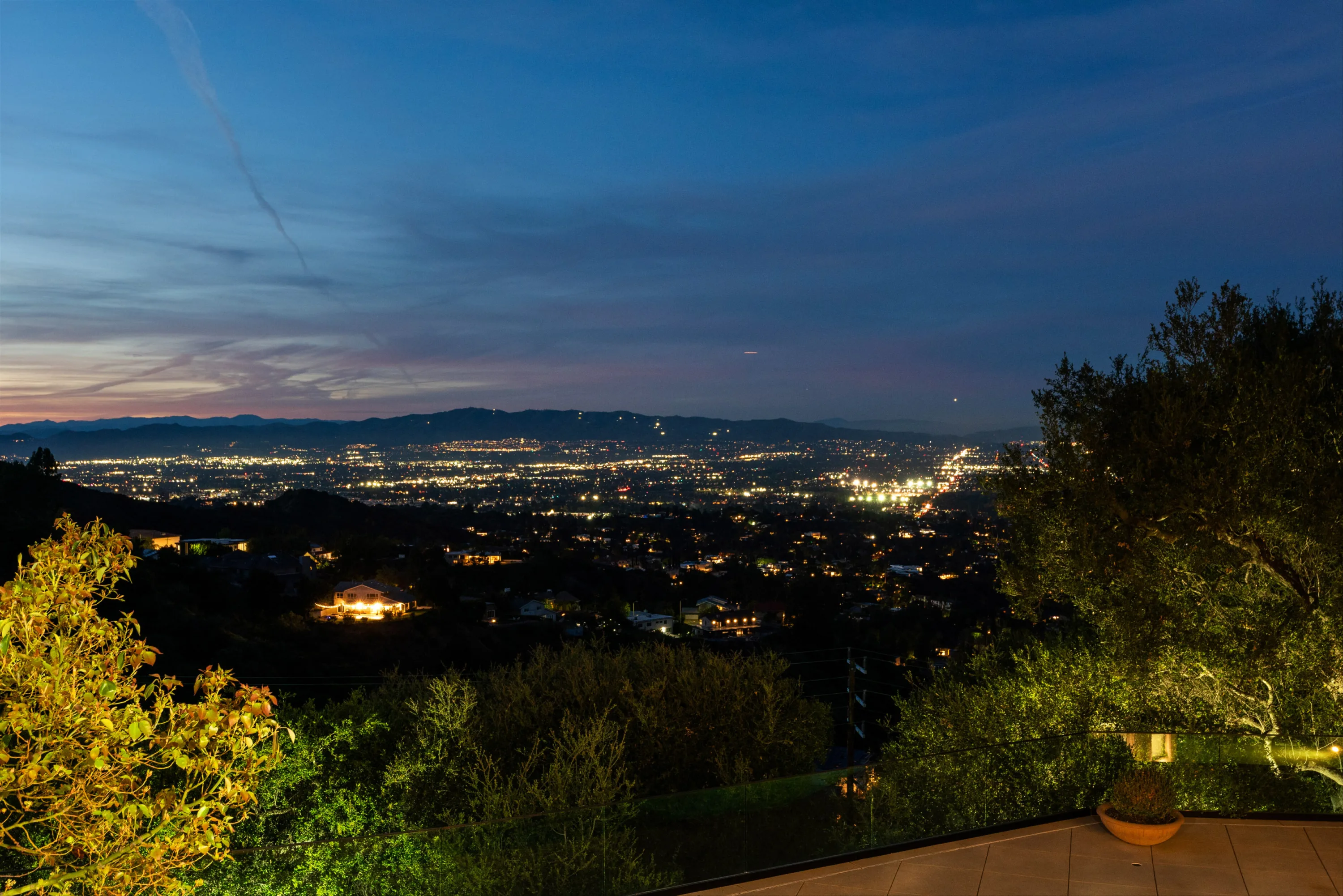 Panoramic city lights and distant ridgelines from the glass-railed terrace after sunset