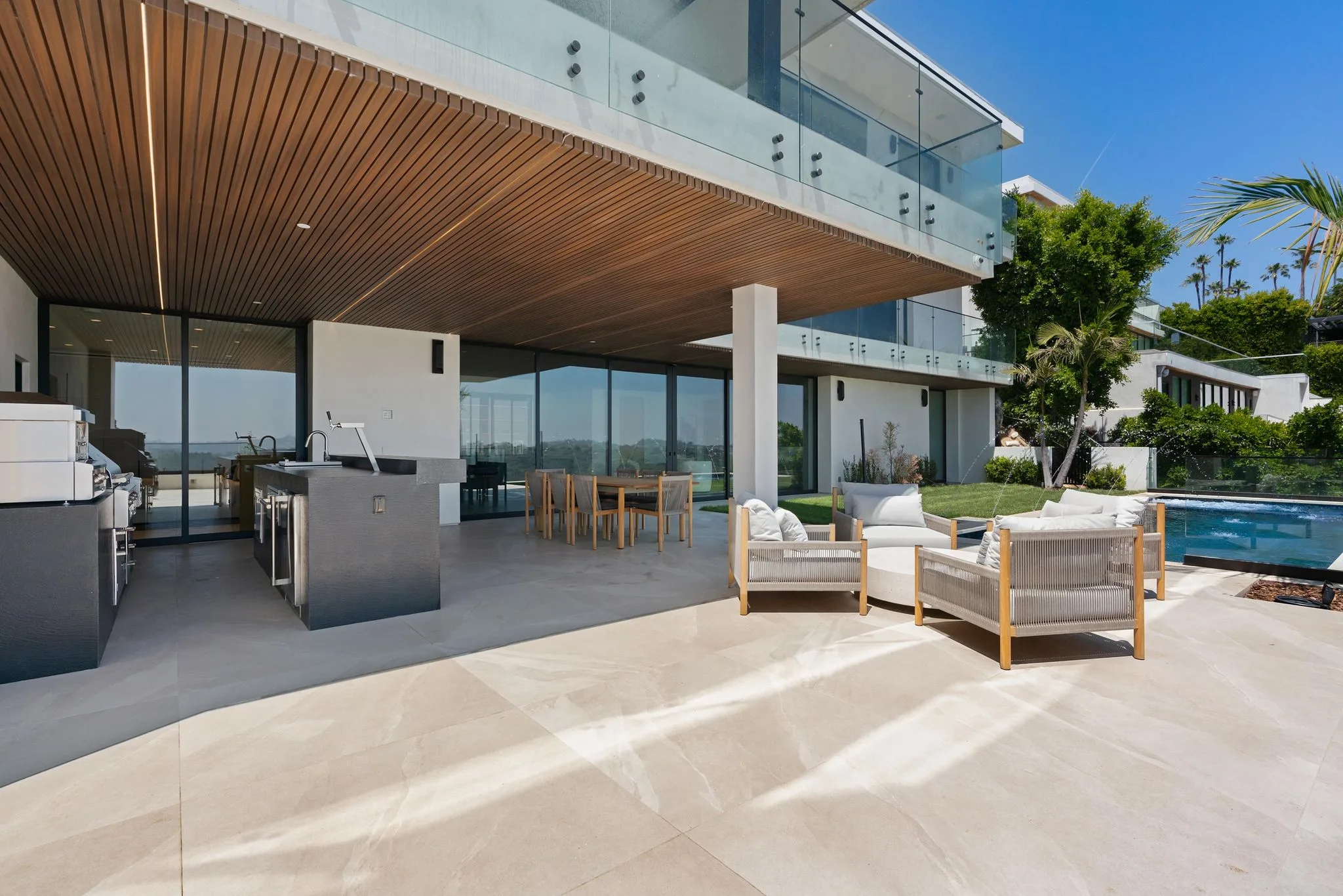 Sun-washed pool terrace with outdoor kitchen, teak dining table and rope lounge chairs beside the lap pool