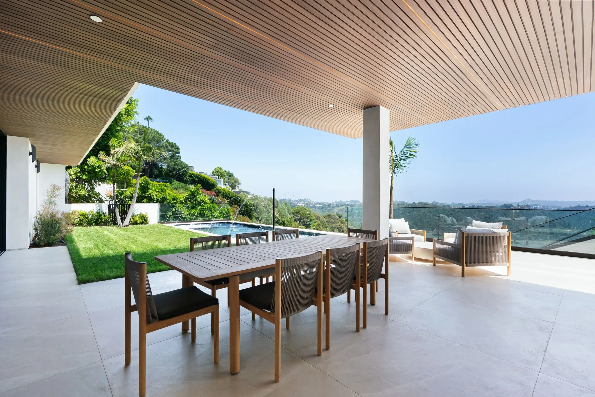 Al fresco dining under the timber soffit, lawn, pool and open canyon panorama beyond the glass balustrade